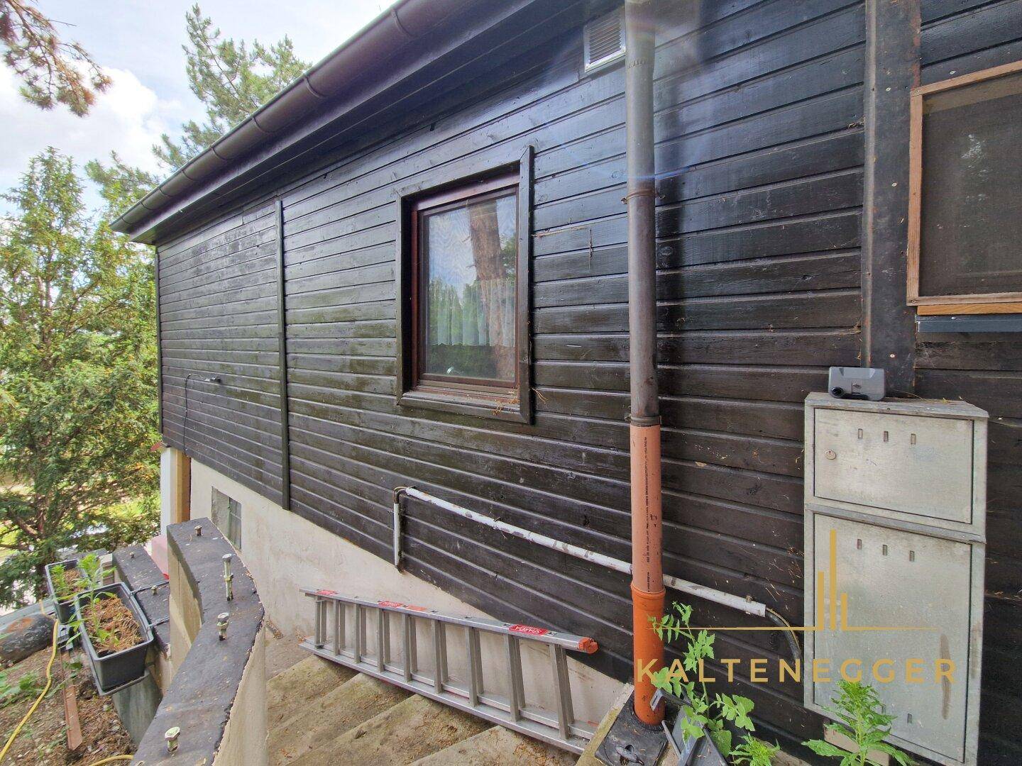 Seitenansicht des Holzhauses mit Fenster und Außeninstallationen.