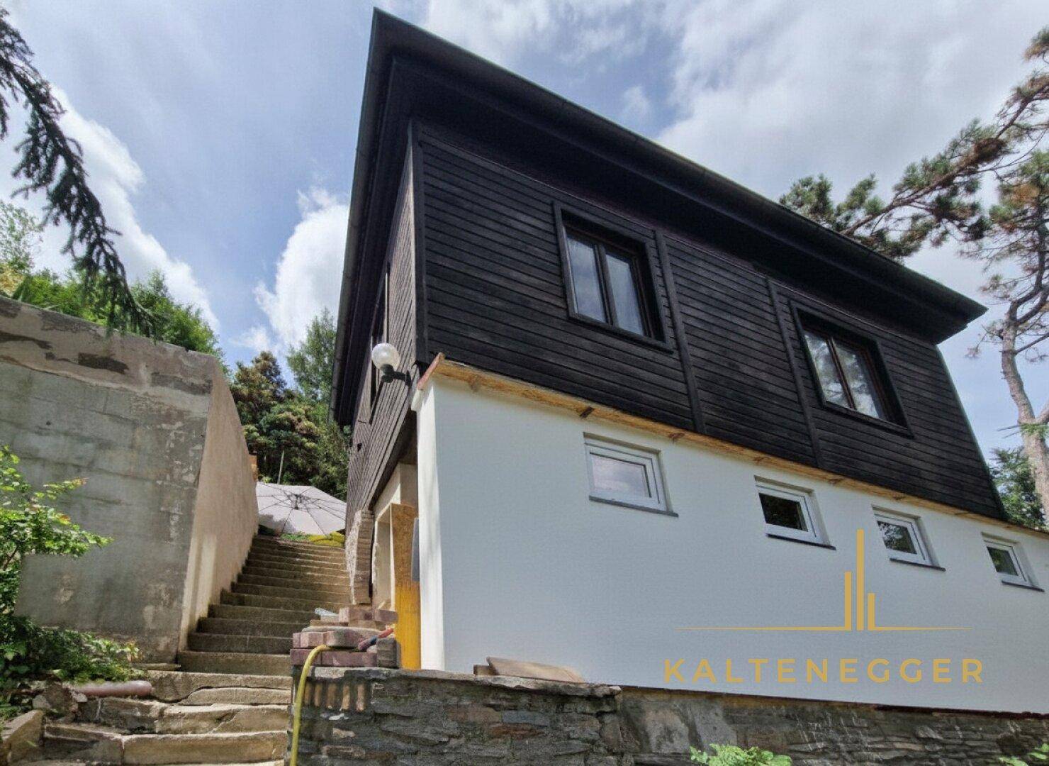Seitenansicht des Hauses mit Außentreppe und dunkler Holzfassade.
