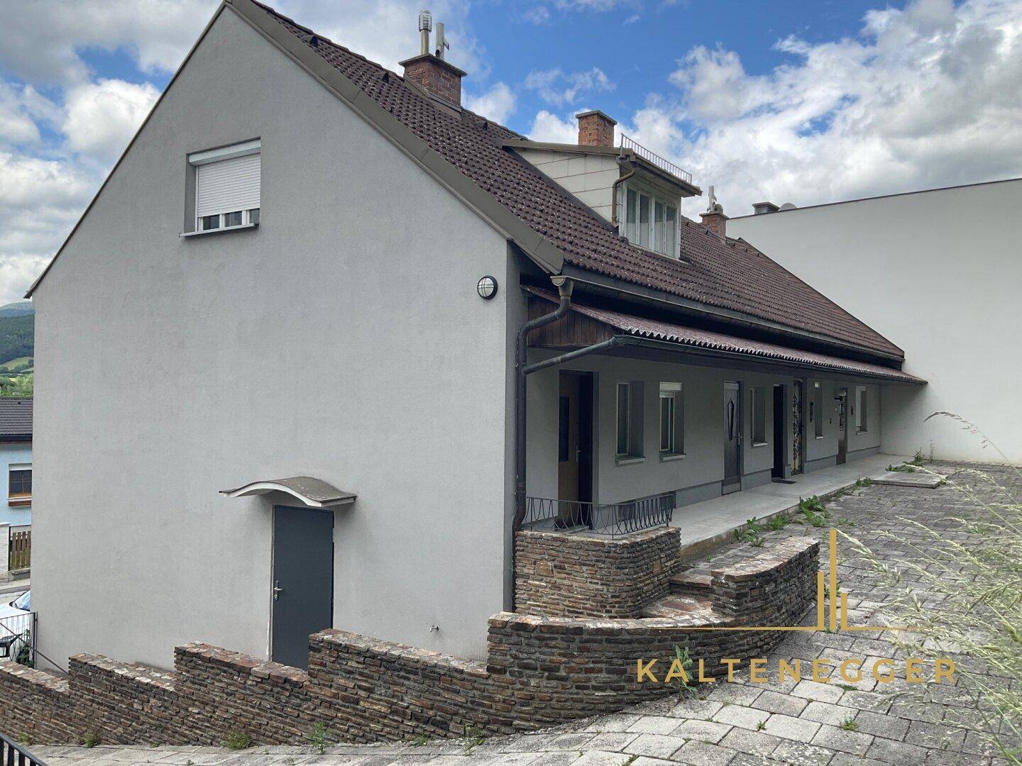 Seitenansicht eines Wohnhauses mit Treppenaufgang und kleiner Überdachung am Eingang.