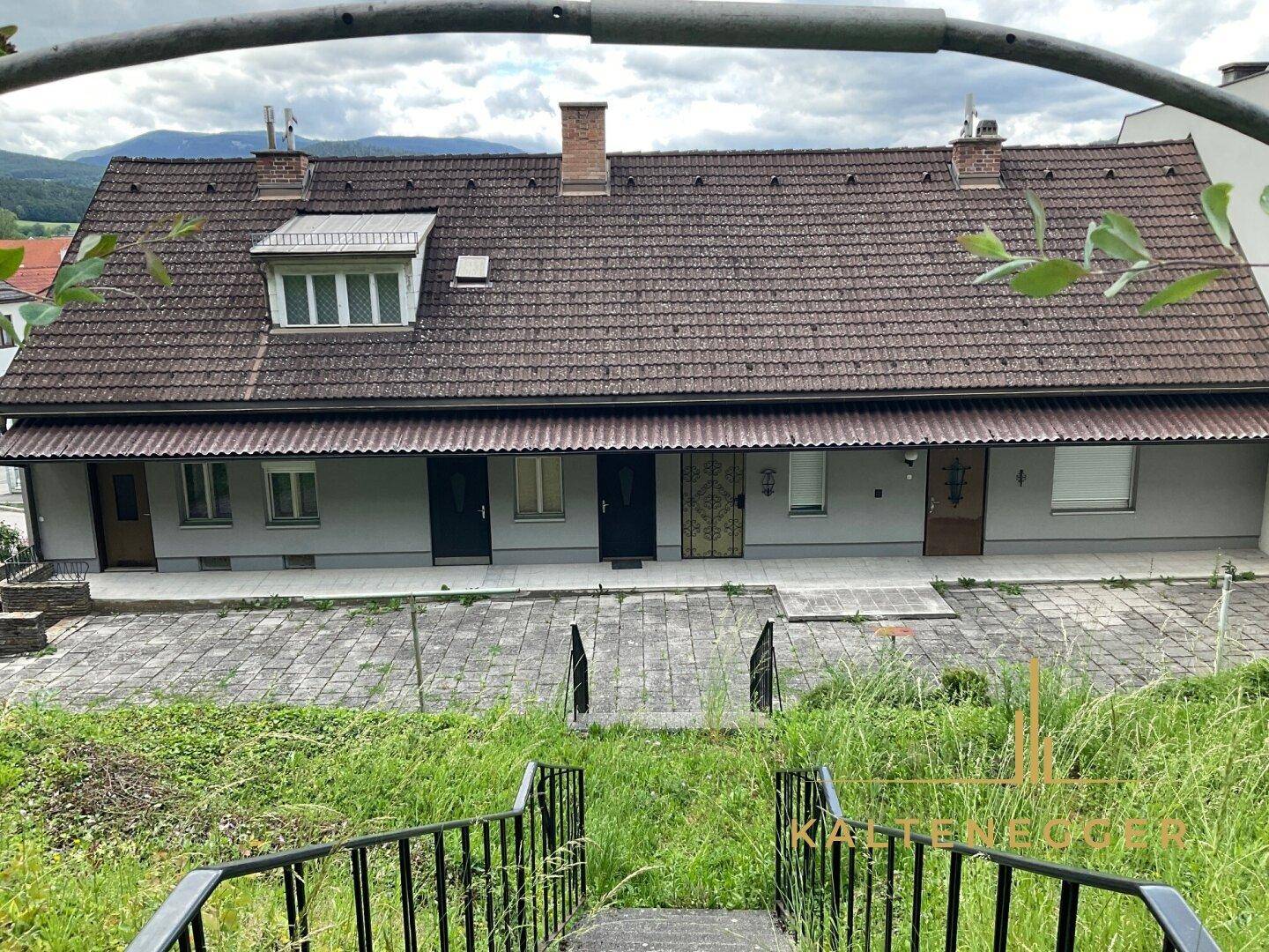 Lange Fassade eines Wohnhauses mit mehreren Eingängen und einem Dach mit Ziegeln.