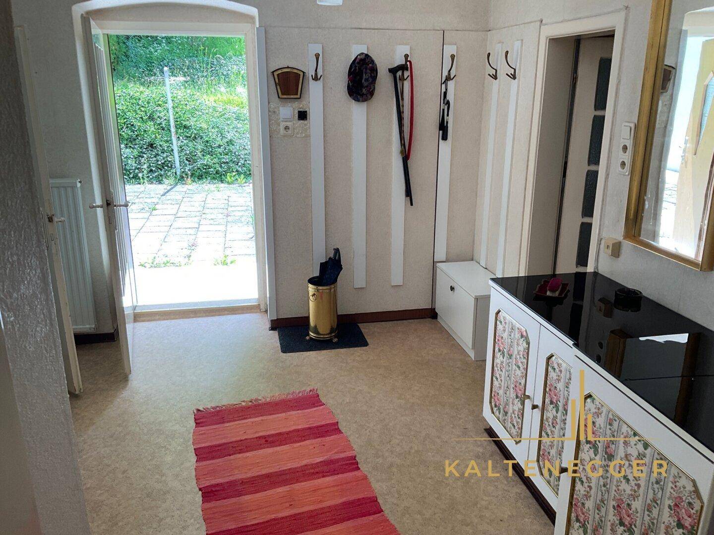 Heller Eingangsbereich mit Garderobe, Spiegel und Zugang zum Außenbereich.