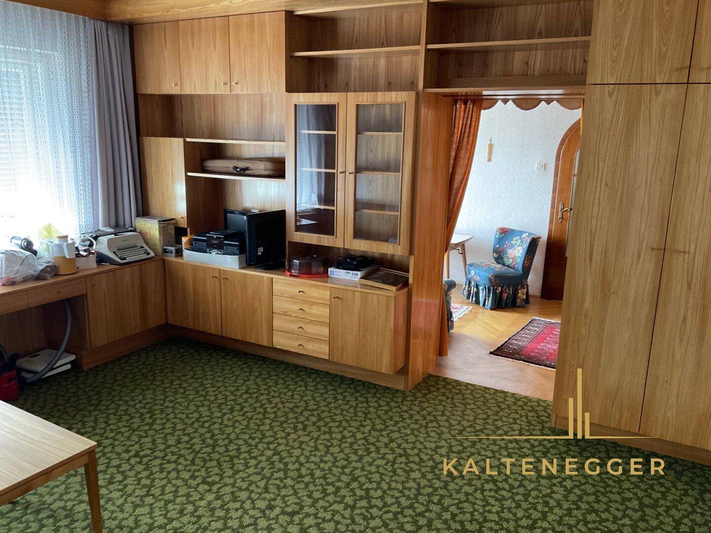 Arbeitszimmer mit Holzmöbeln, Teppichboden und Blick in einen angrenzenden Raum.