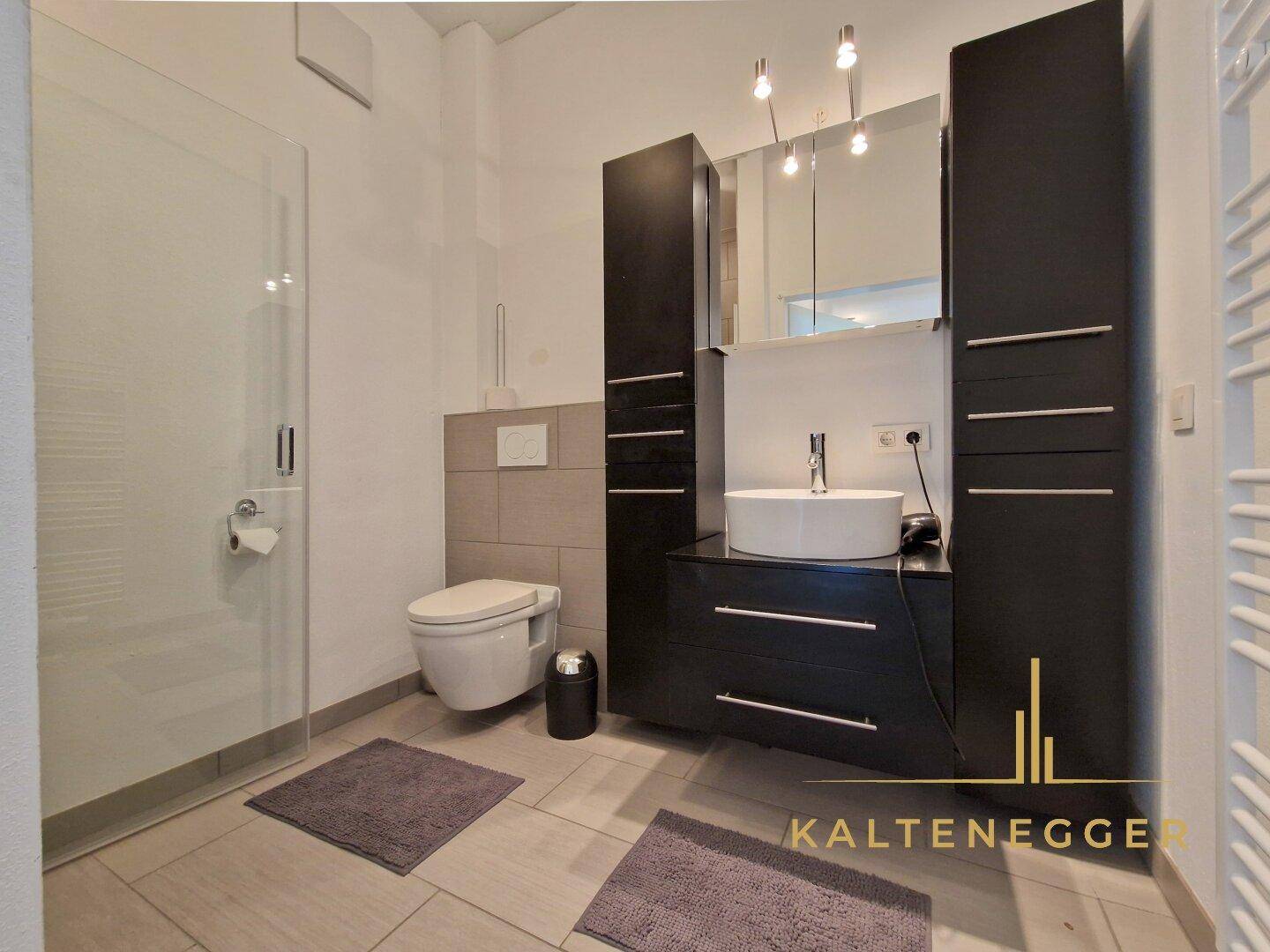 Modernes Badezimmer mit dunklen Schränken, runder Waschschale und begehbarer Dusche.