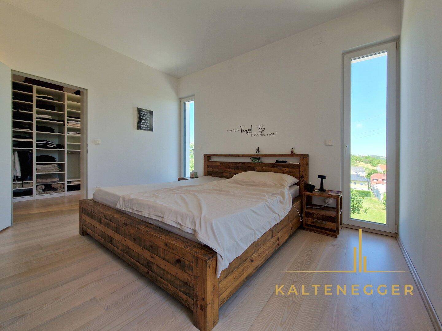 Gemütliches Schlafzimmer mit Holzbett, hellen Holzböden und hohen Fenstern mit Ausblick.
