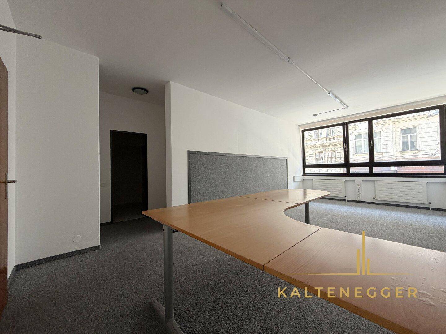 Geräumiges Büro mit dunklem Teppichboden, großen Fenstern und einem geschwungenen Schreibtisch.
