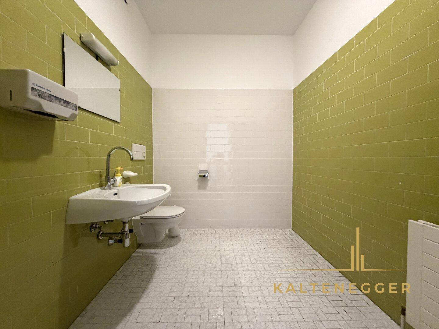 Toilette mit grünen und weißen Wandfliesen, einem Waschbecken und einem wandhängenden WC.