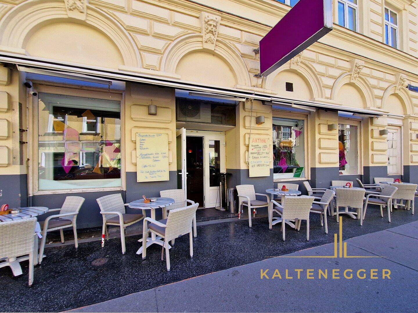 Außenbereich eines Cafés mit Tischen und Stühlen auf dem Bürgersteig vor einer klassischen Fassade.