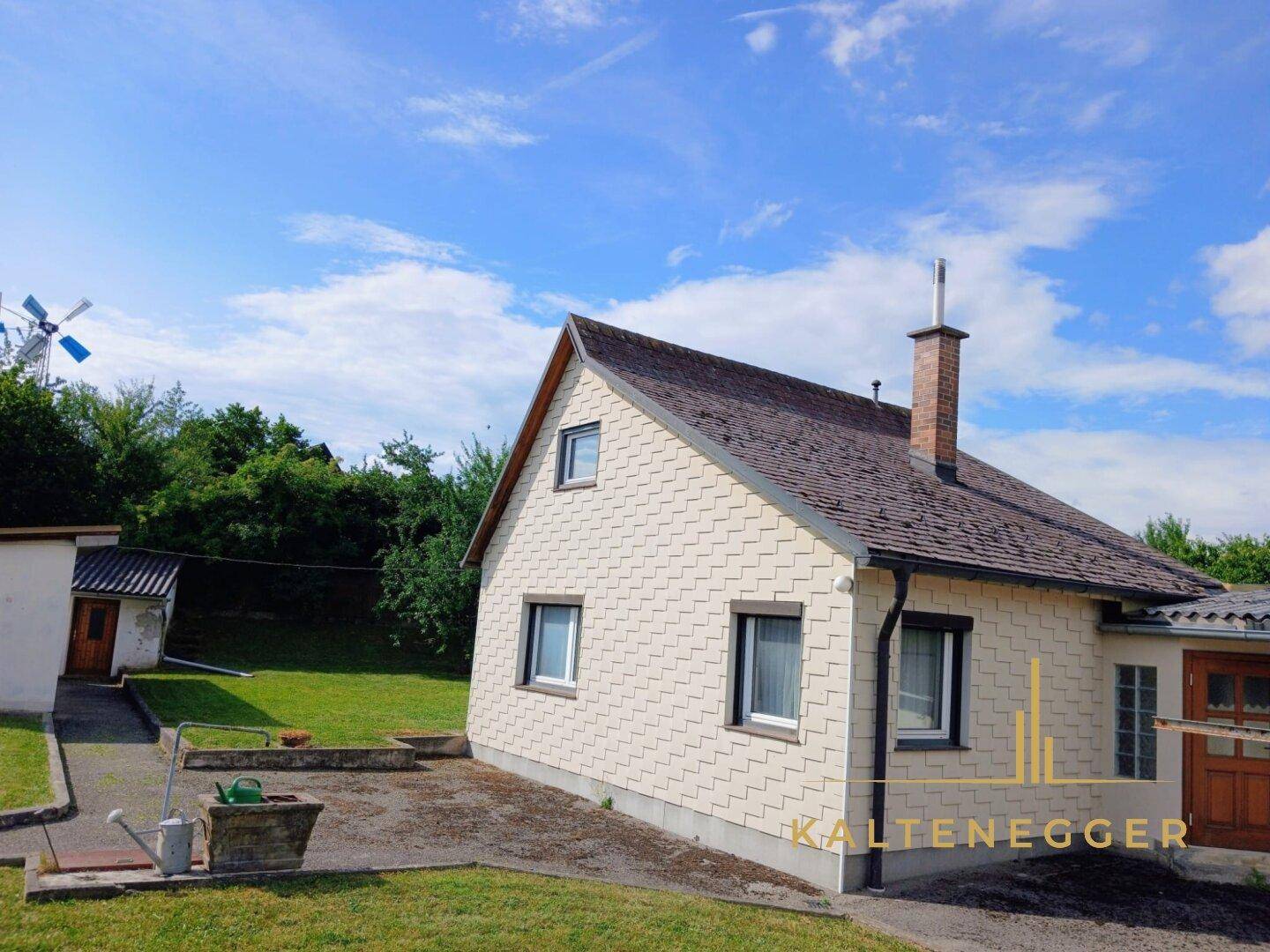 Gesamtansicht des Hauses mit Satteldach, Kamin und dem weitläufigen Grundstück bei Sonnenschein.