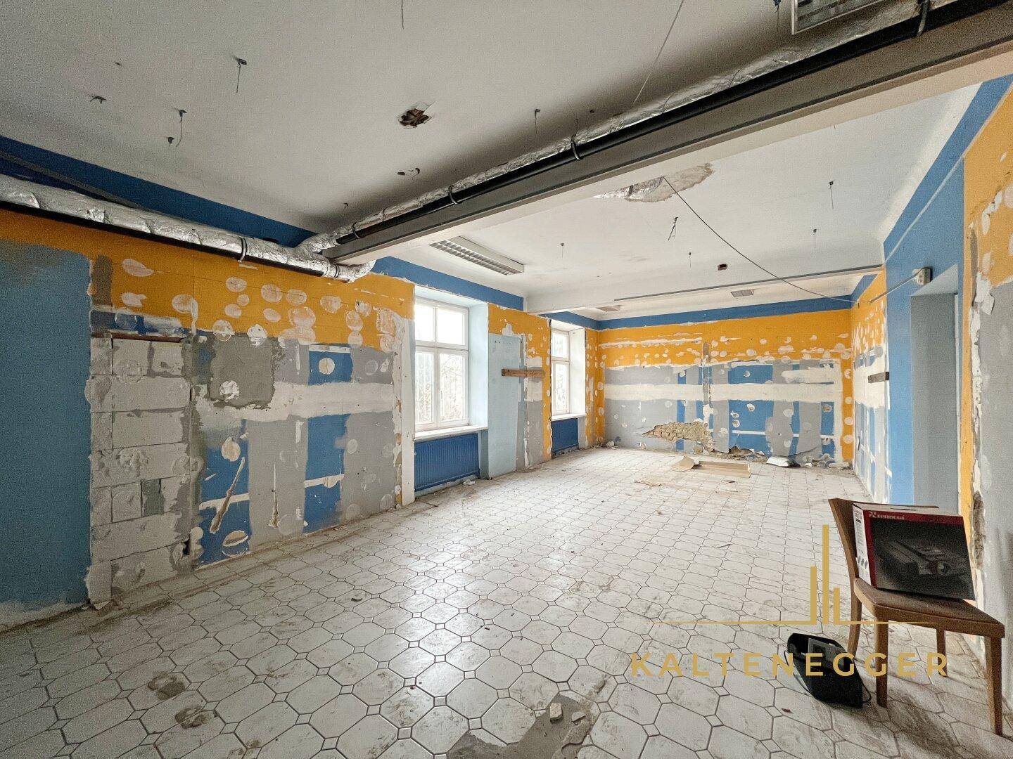 Gewerbefläche mit teilweise abgehängter Decke, Fliesenboden und Wänden in Renovierungszustand.