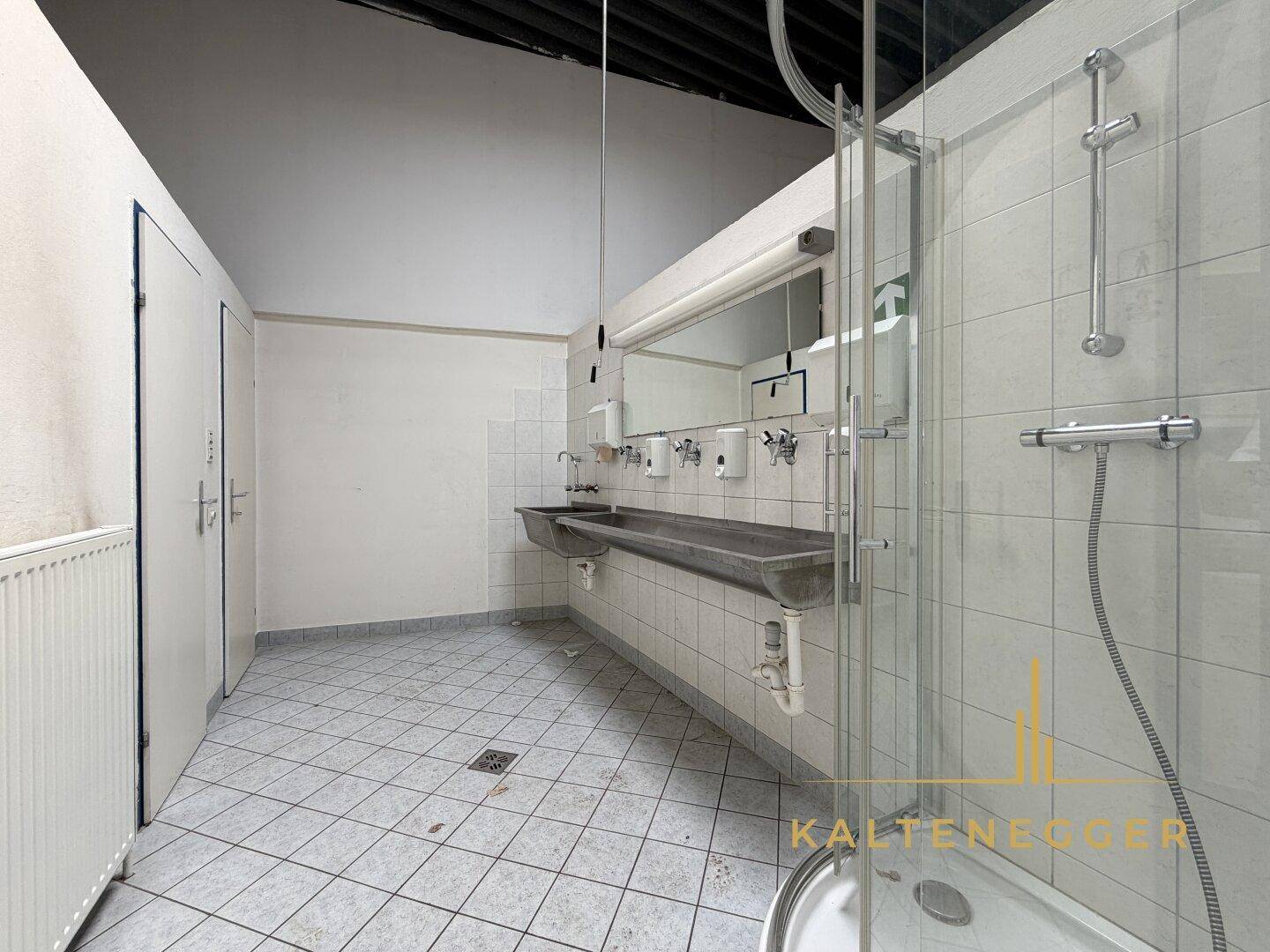 Geräumiger Waschraum mit mehreren Waschbecken, Dusche und gefliestem Boden, ideal für Mitarbeiter.