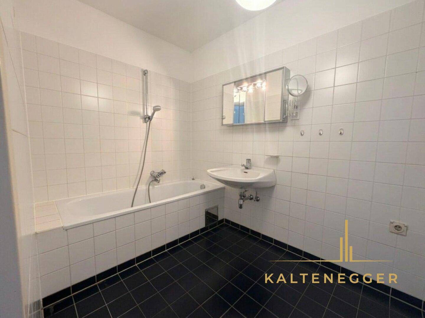 Badezimmer mit weißen Wandfliesen, dunklem Boden und Badewanne mit Duschfunktion.