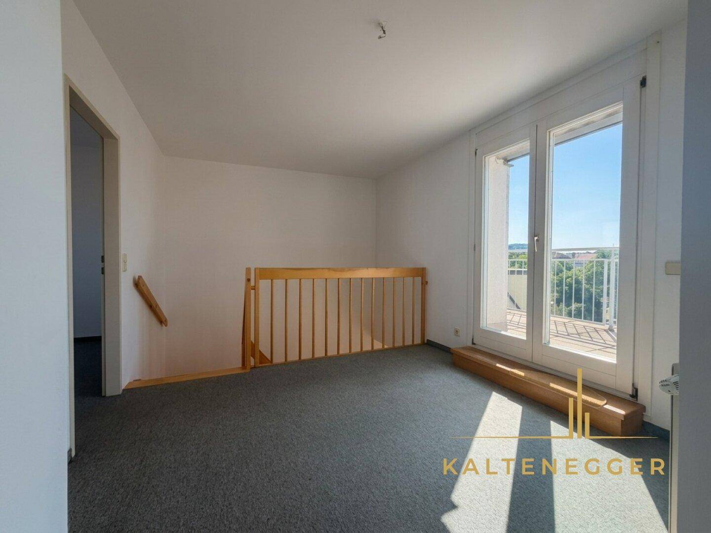 Heller Raum mit Teppichboden, Treppengeländer und Zugang zu einer Fenstertür.