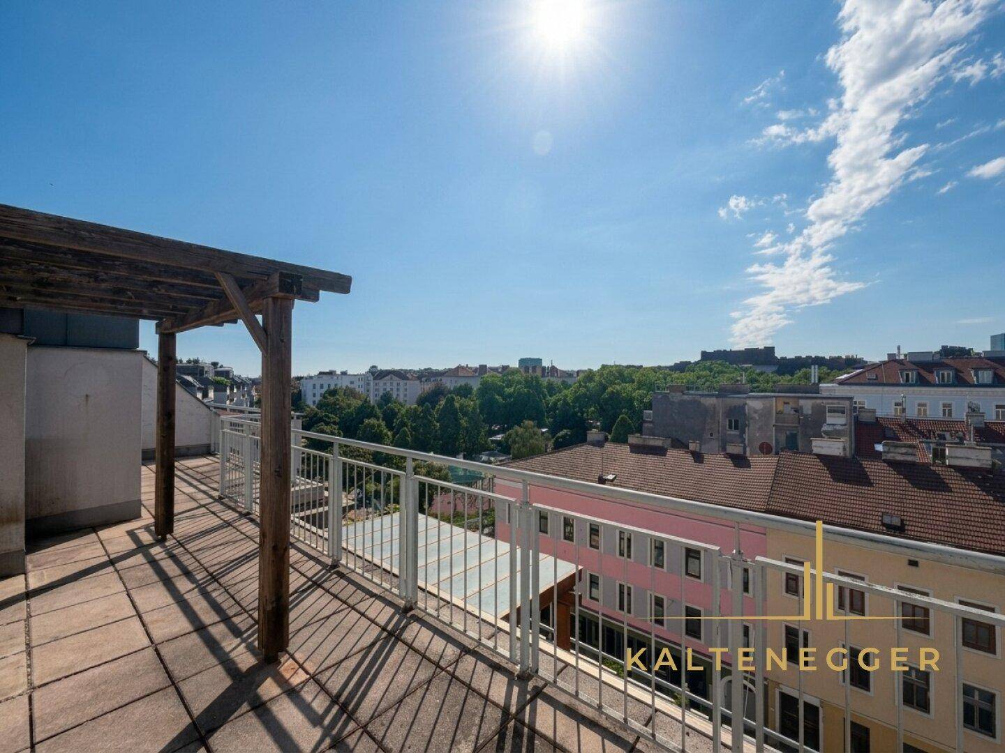 Sonnige Dachterrasse mit weitem Stadtblick und Metallgeländer unter blauem Himmel.