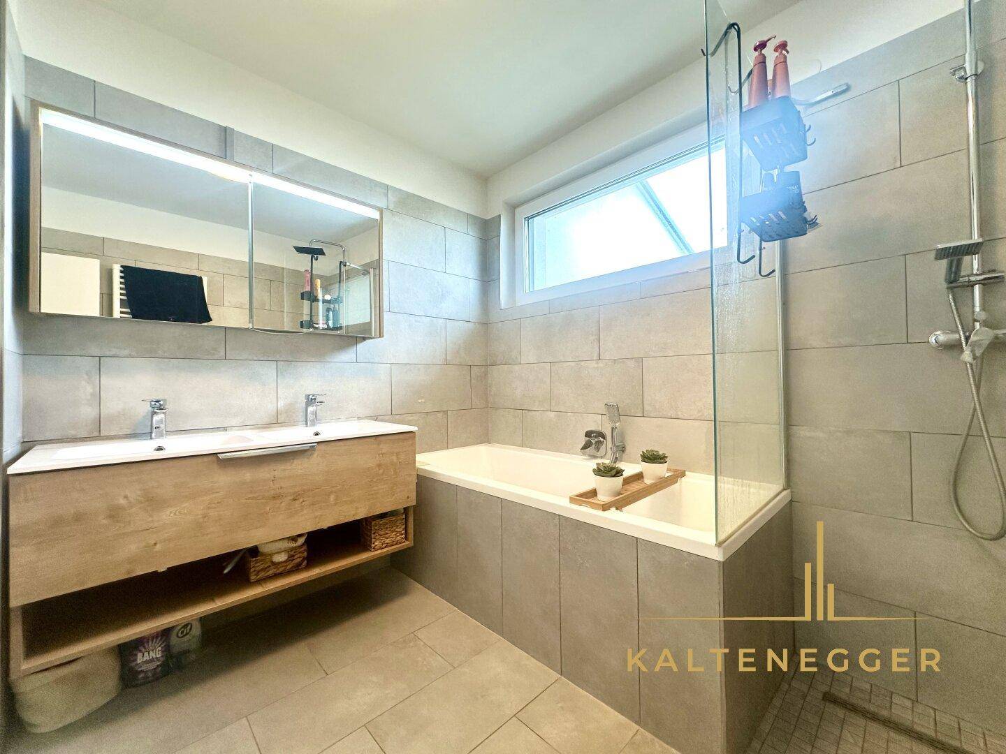Modernes Badezimmer mit Doppelwaschbecken, Badewanne und ebenerdiger Dusche, hell gefliest.