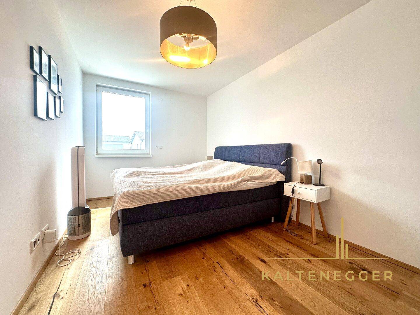 Gemütliches Schlafzimmer mit Holzboden, großem Bett und viel Tageslicht durch das Fenster.