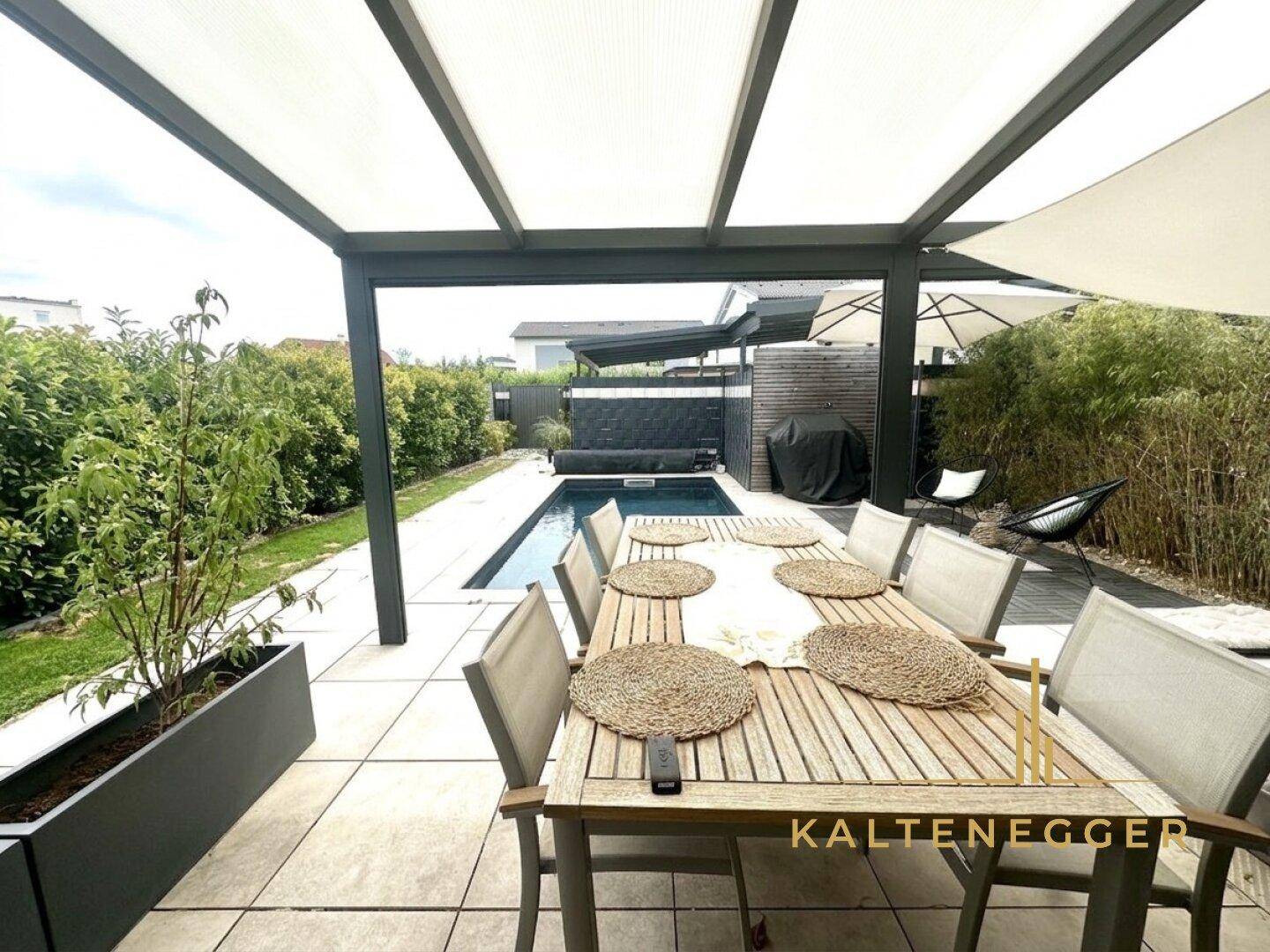Überdachter Essbereich im Freien mit großem Holztisch und Blick auf den privaten Pool und Garten.