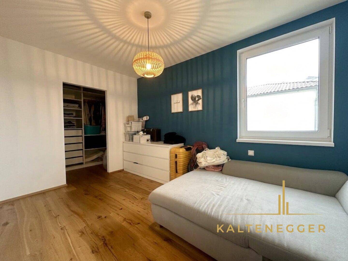 Helles Schlafzimmer mit Holzboden, farbiger Akzentwand und offenem begehbarem Kleiderschrank.