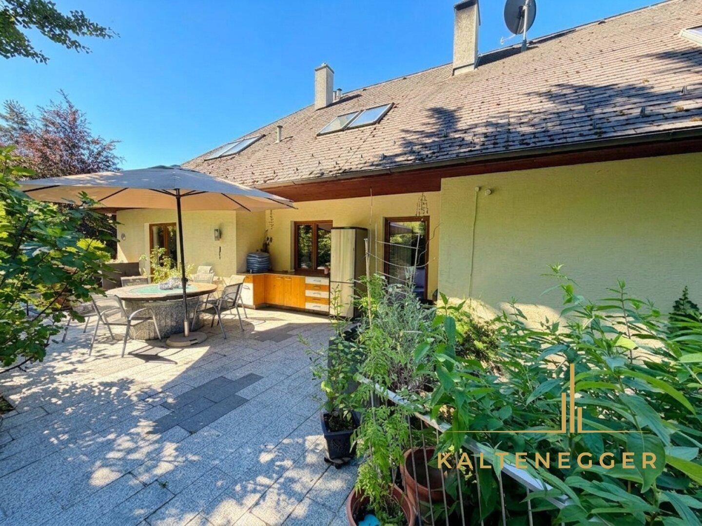 Große gepflasterte Terrasse mit Sonnenschirm, Sitzgelegenheiten und Blick ins Grüne.