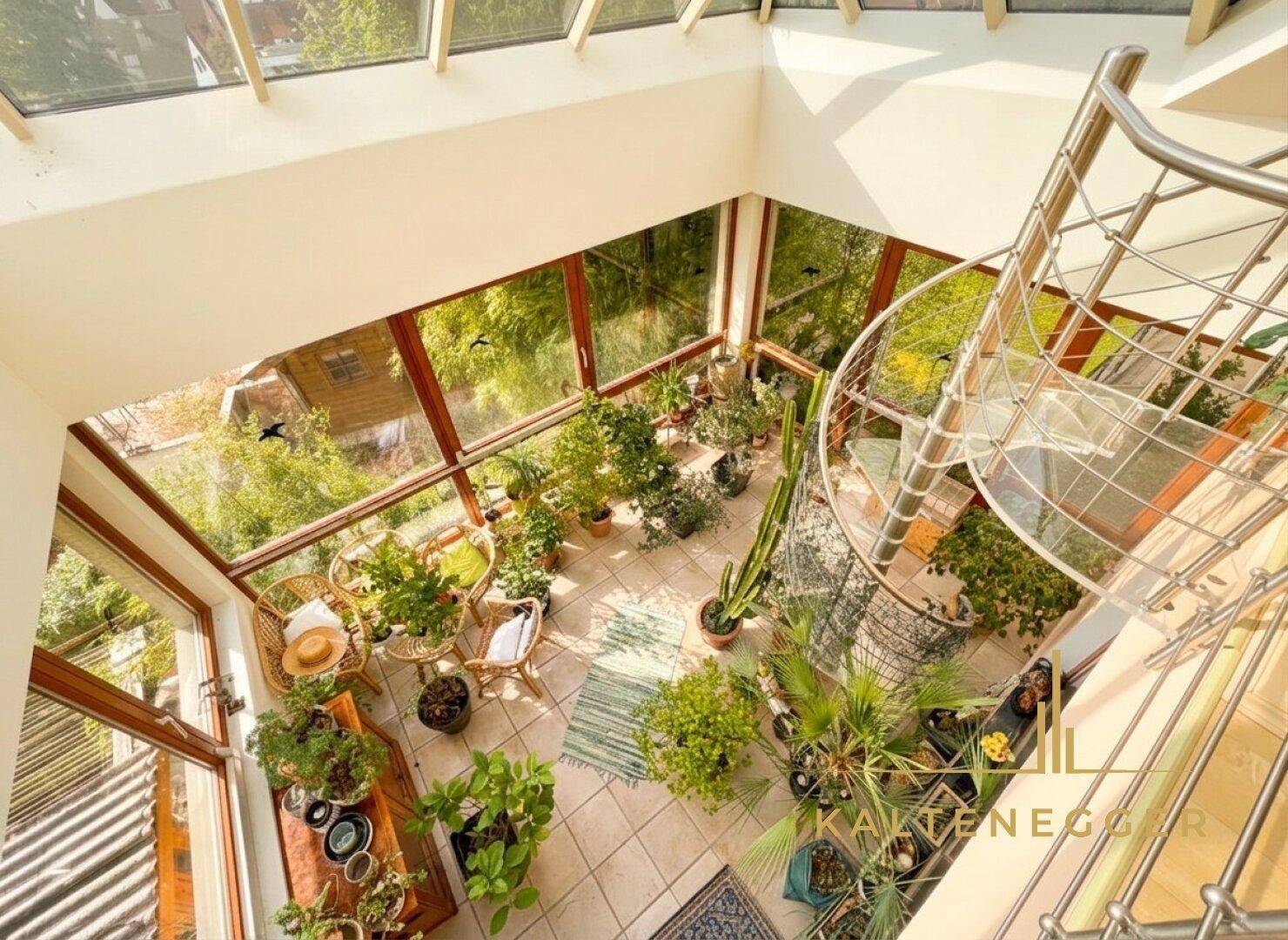 Geräumiger Wintergarten mit Wendeltreppe, vielen Pflanzen und hellem Fliesenboden.