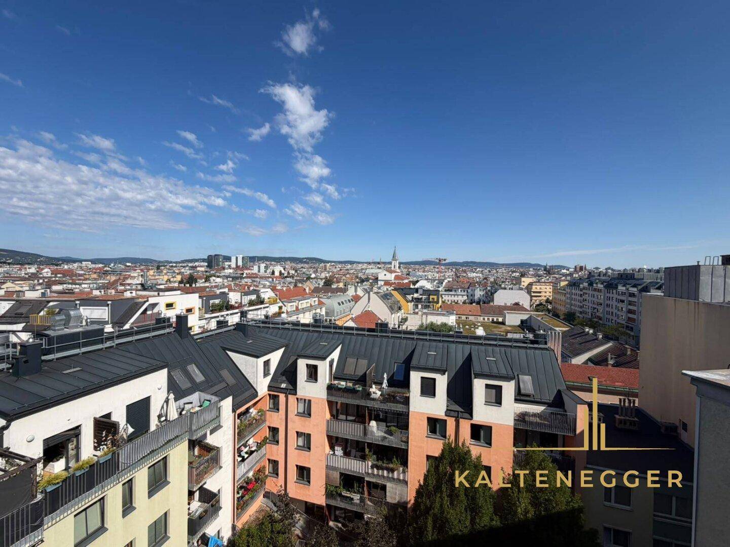 Panoramablick über die Stadt mit Wohngebäuden und grünen Hügeln im Hintergrund.