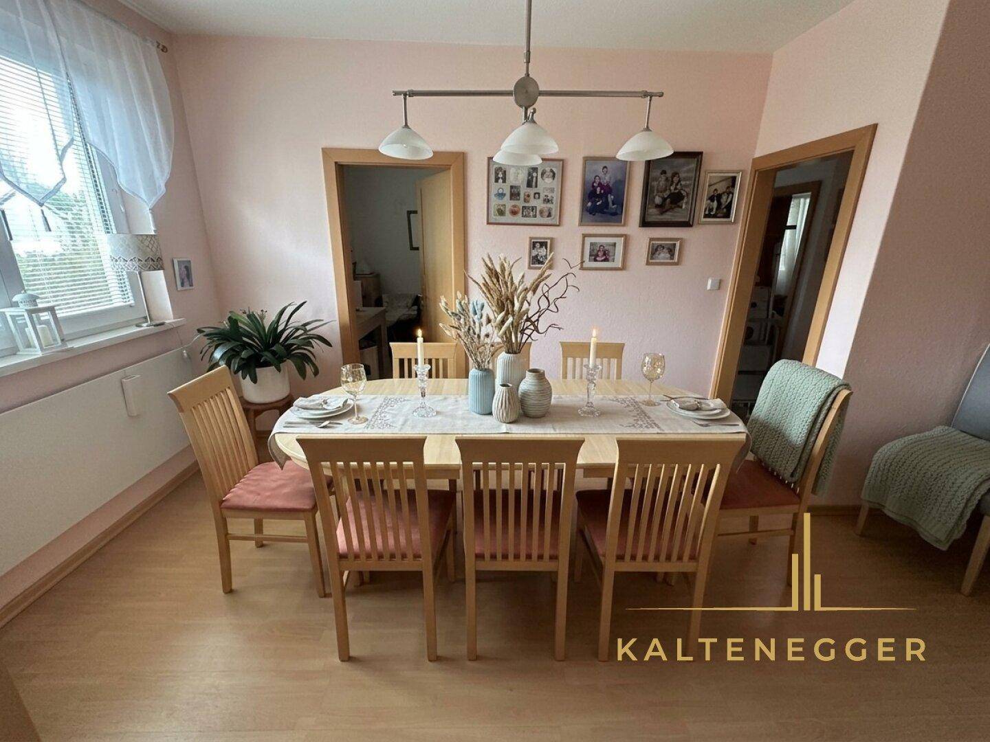 Heller Essbereich mit großem Holztisch, sechs Stühlen und Bildern an den zartrosa Wänden.