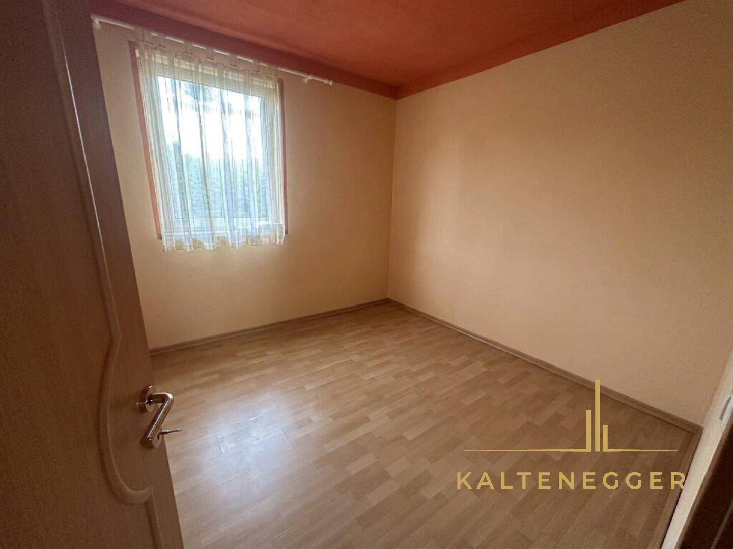 Leeres Zimmer mit hellem Laminatboden, orangefarbenen Wänden und einem Fenster für natürliches Licht.