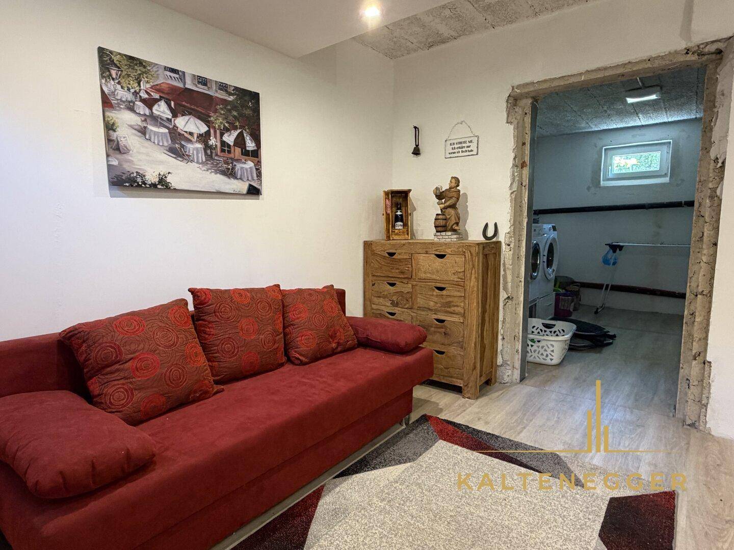 Gemütlicher Kellerraum mit Sofa und Schrank, angrenzend an einen Waschraum.