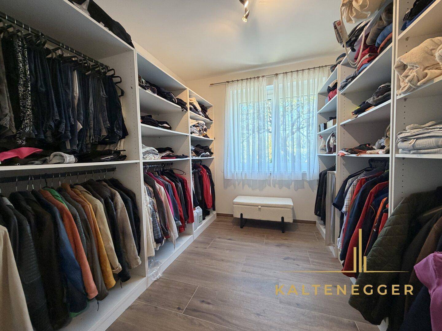 Geräumiger begehbarer Kleiderschrank mit viel Stauraum und einem Fenster für Tageslicht.