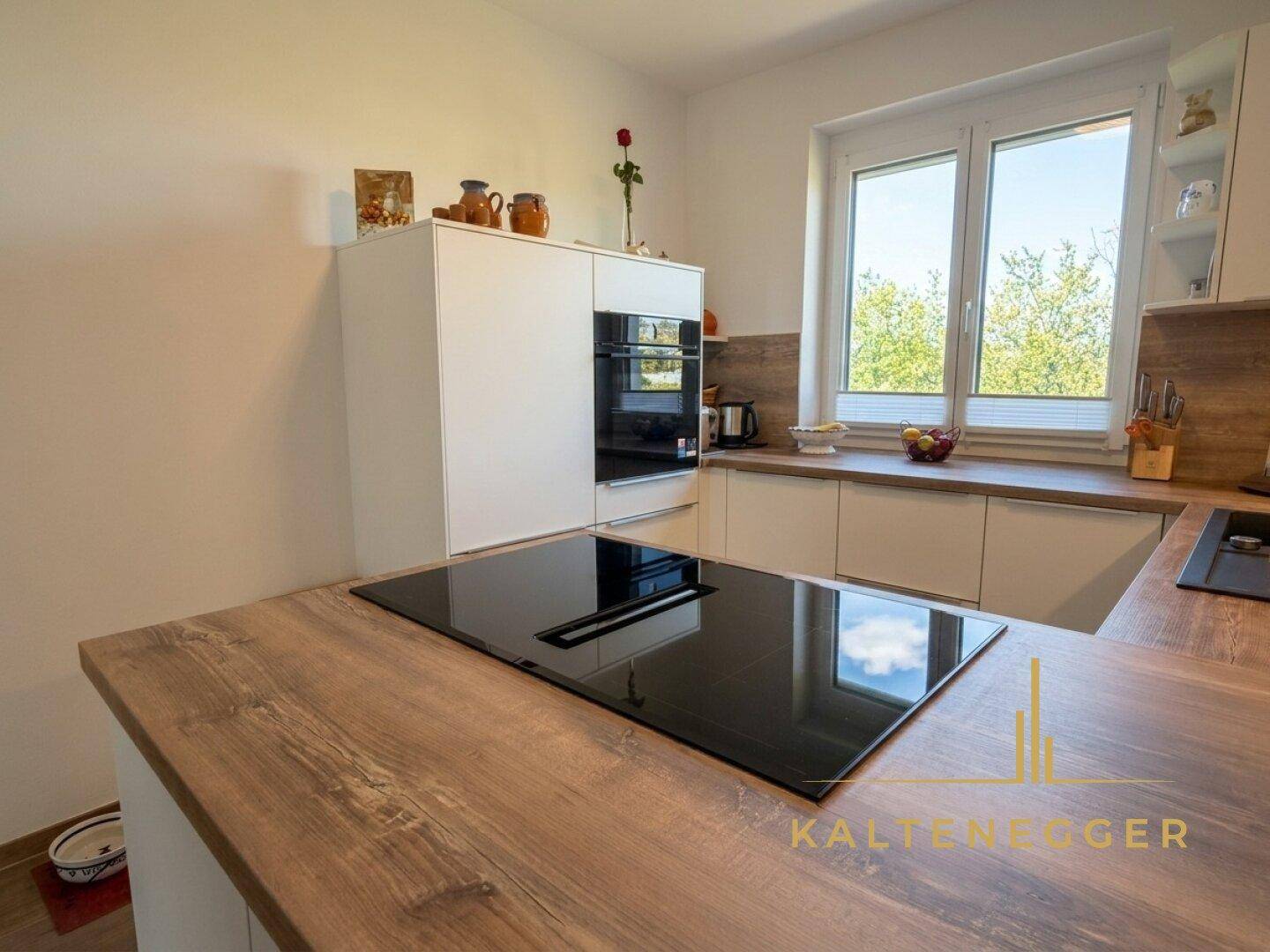 Heller Küchenbereich mit integriertem Backofen und Mikrowelle, sowie Fenster mit Ausblick.