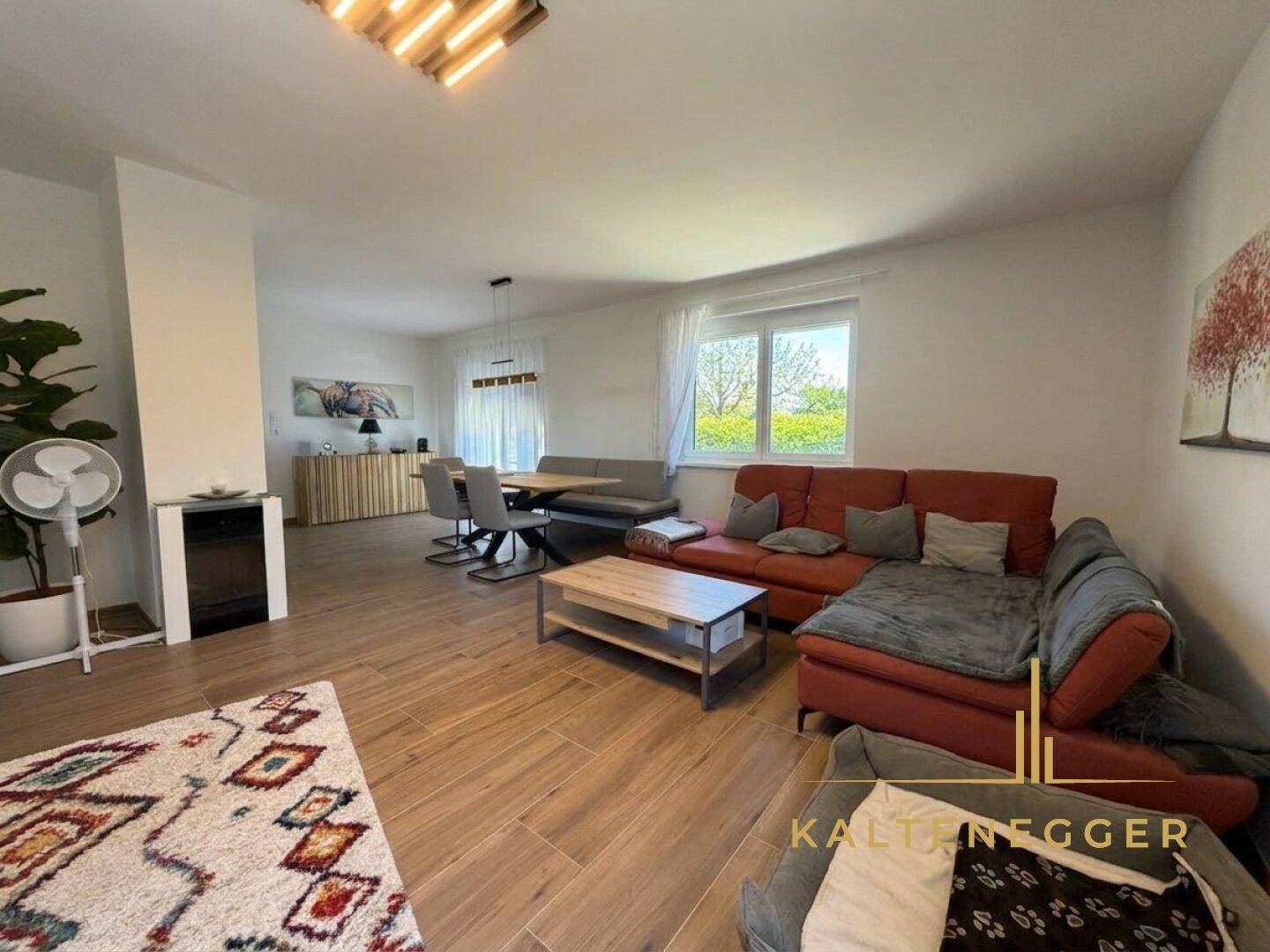 Heller Wohnbereich mit großem Sofa, Holzboden und Fenster, das viel Tageslicht hereinlässt.