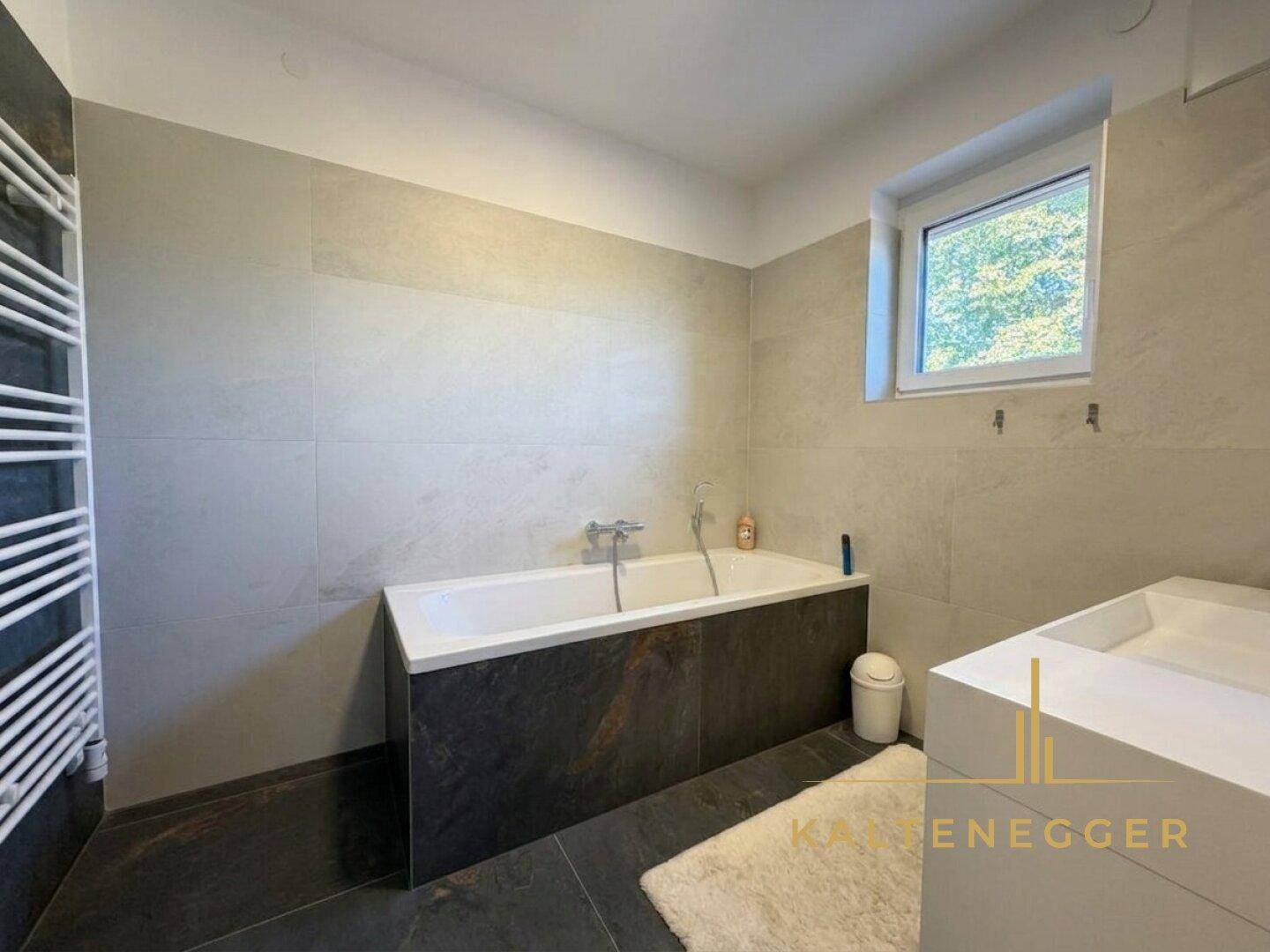 Modernes Badezimmer mit Badewanne, Einzelwaschbecken und beheiztem Handtuchhalter.