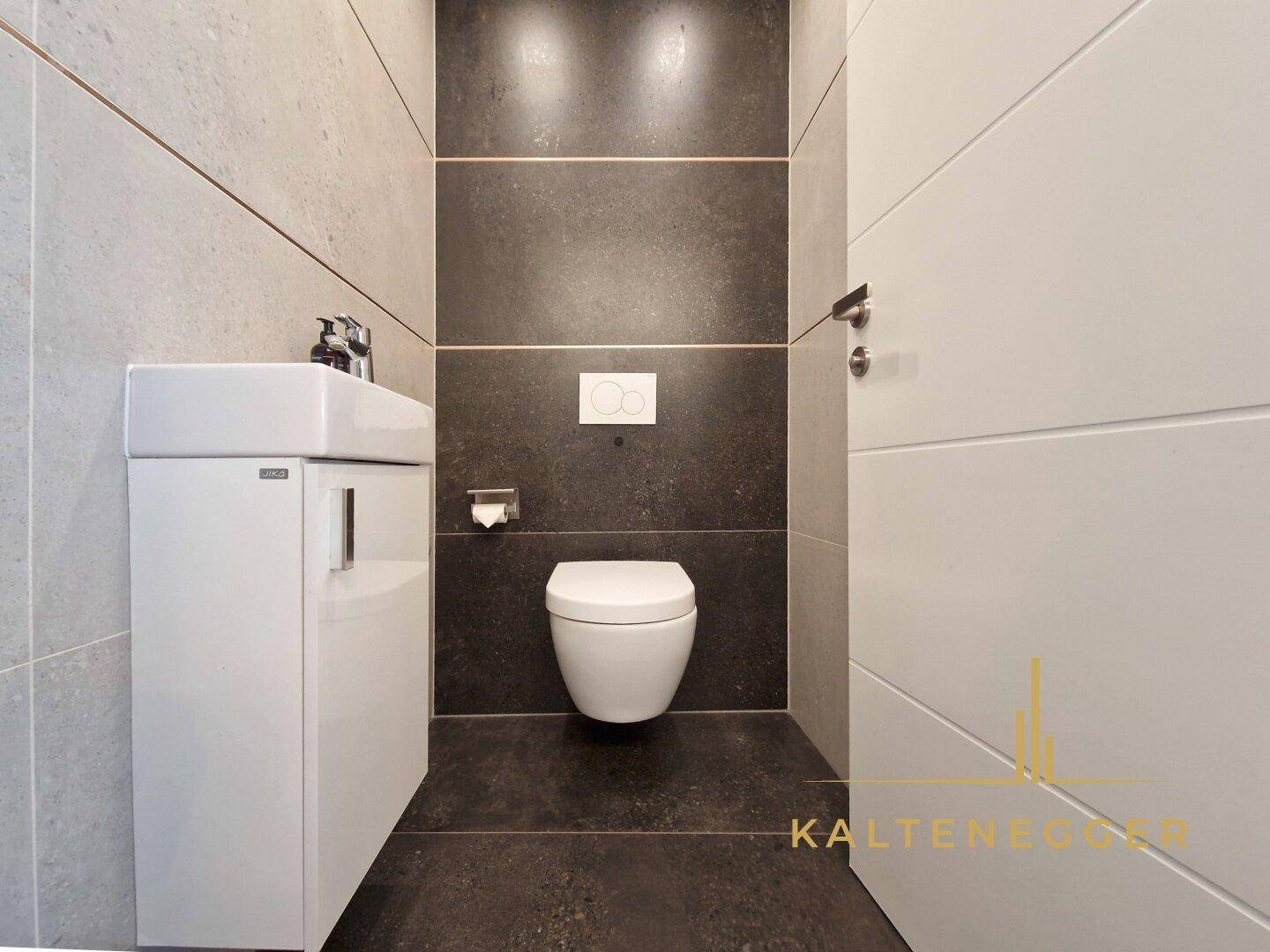 Modernes Gäste-WC mit Wand-WC und kleinem Waschtisch in dunklen und hellen Fliesen.