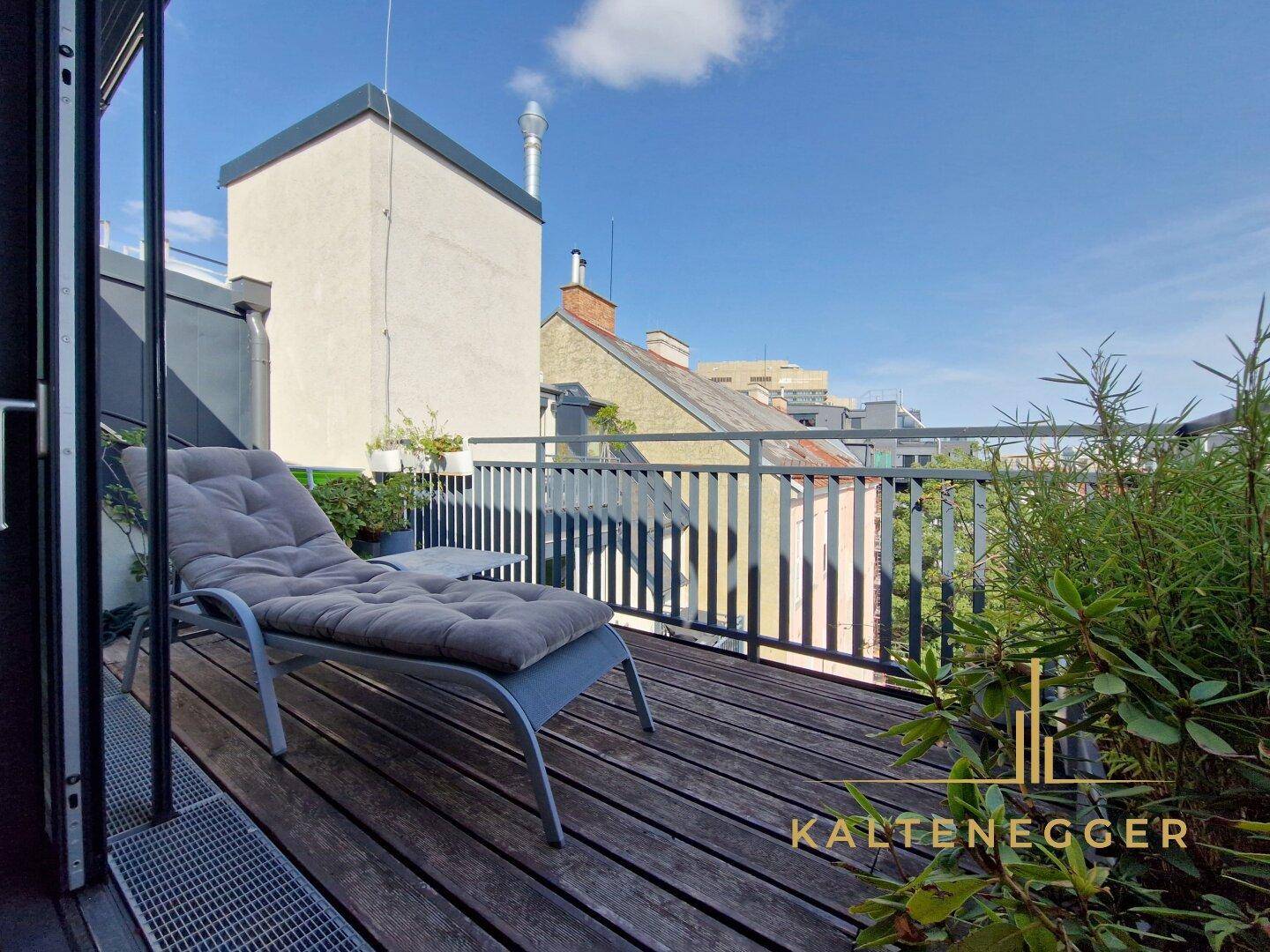 Sonnige Dachterrasse mit Holzbelag, Liegestuhl und Blick über die Stadt.