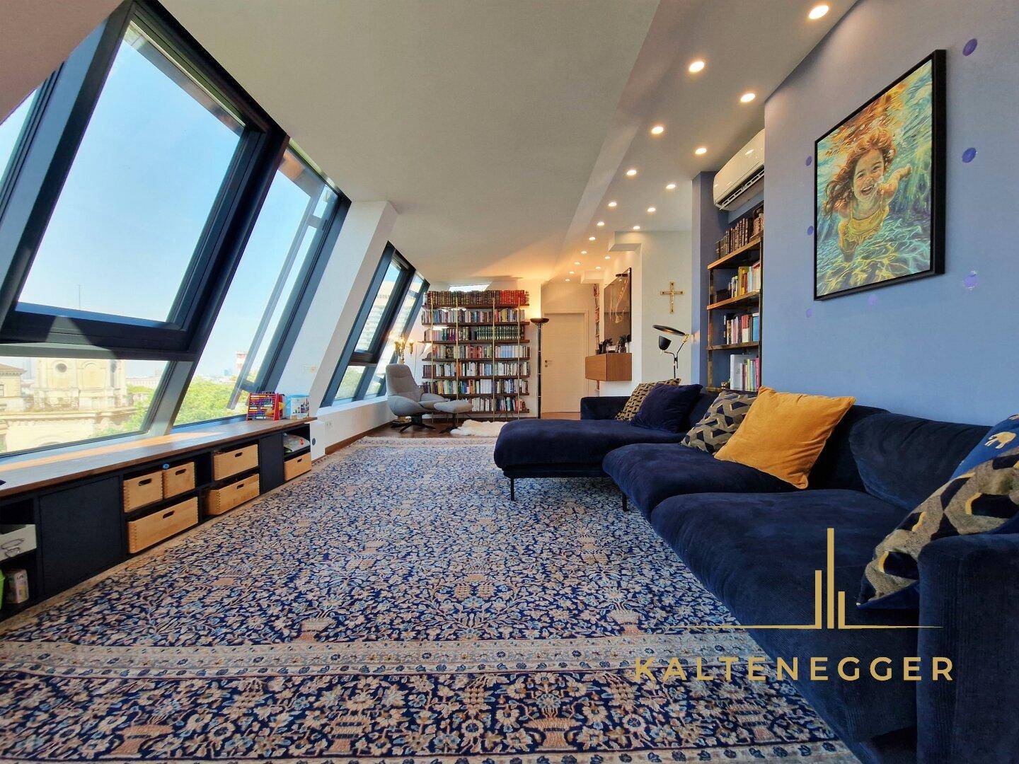 Großzügiges Wohnzimmer mit blauer Couch, Bücherregalen und schrägen Fenstern.