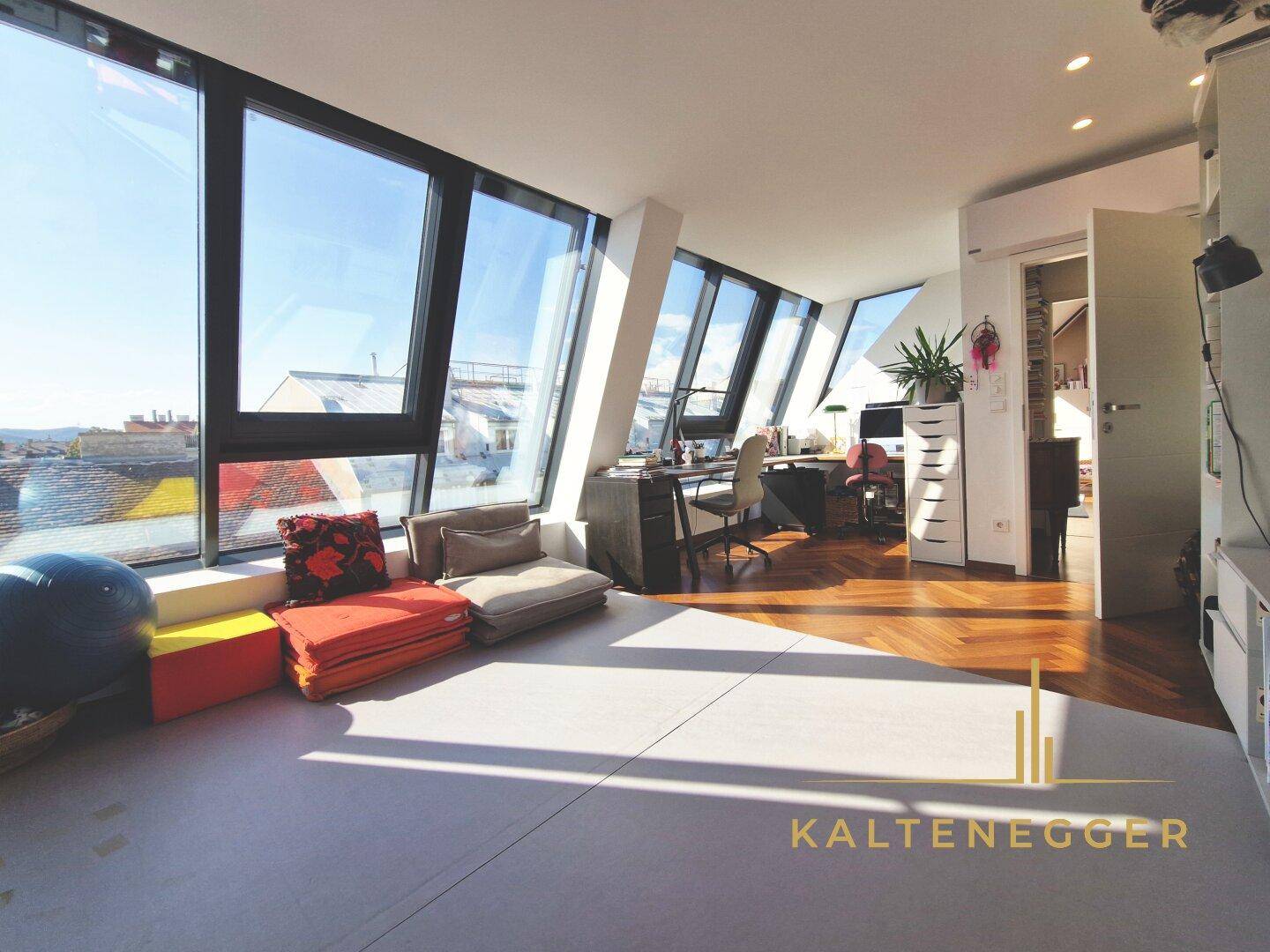 Helles Arbeitszimmer mit großen Schrägfenstern und Blick über die Stadt.