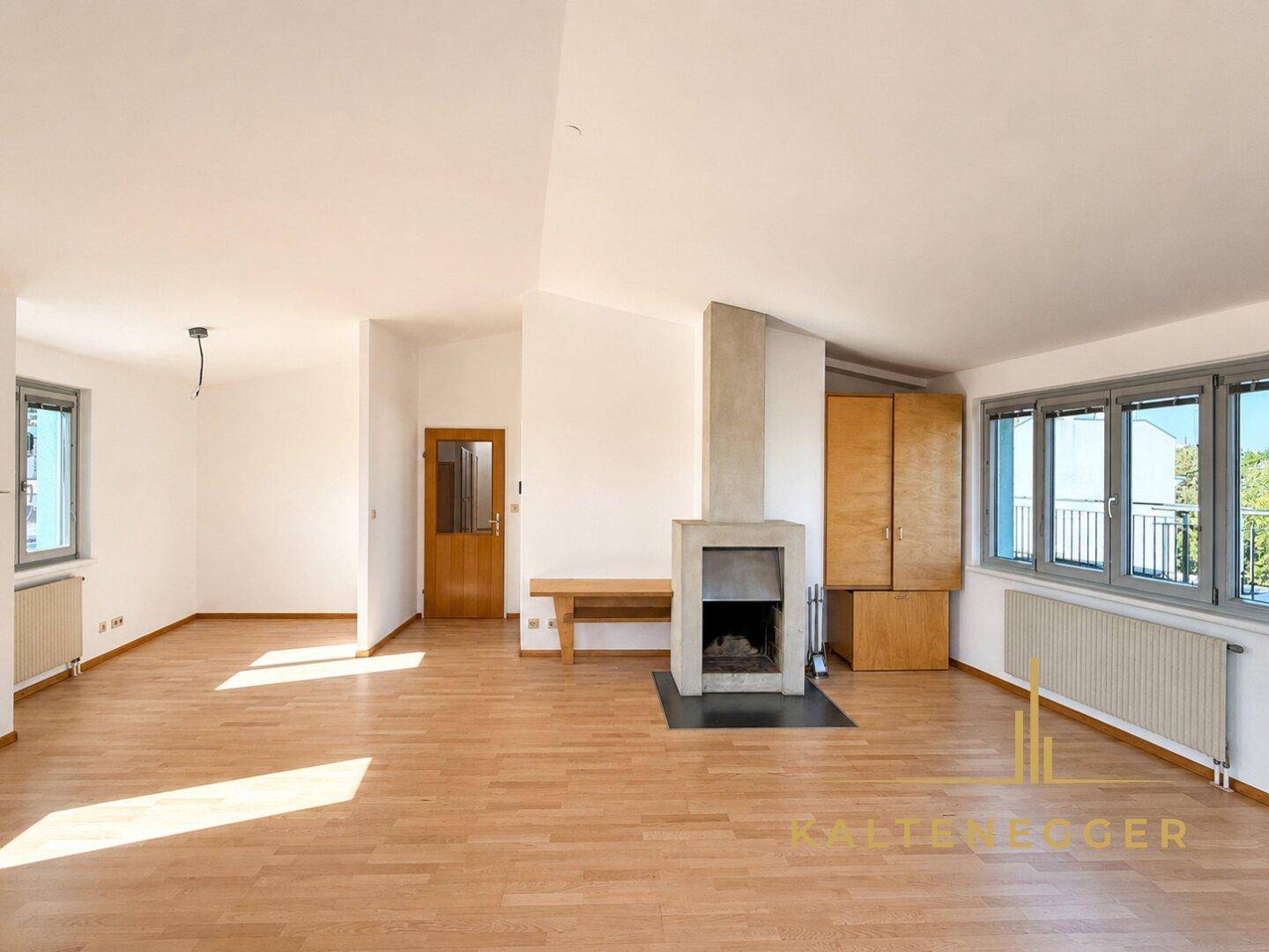 Geräumiges Wohnzimmer mit Holzboden, Kamin und viel Tageslicht durch große Fenster.