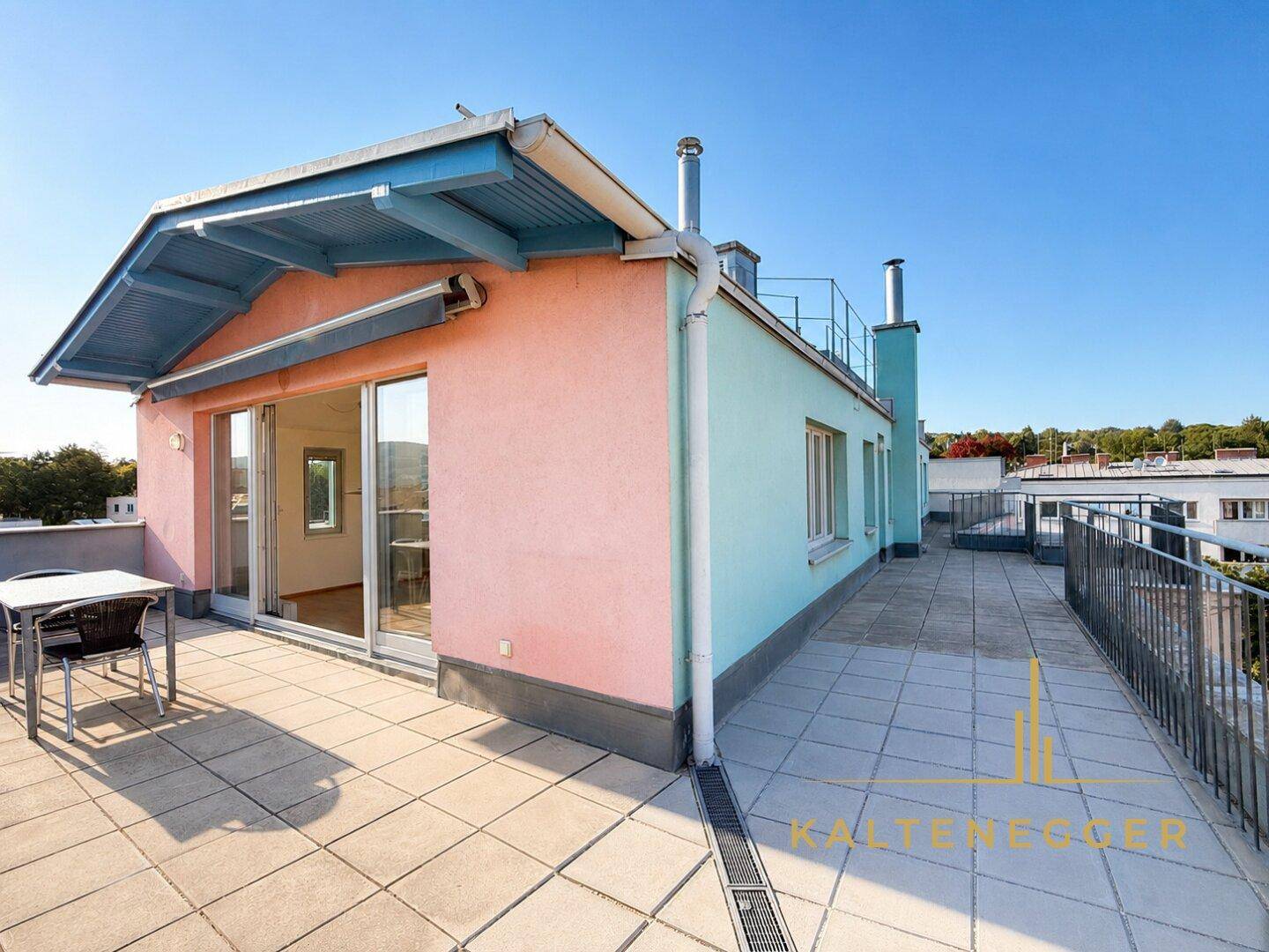 Weitläufige Dachterrasse mit Fliesenboden und farbenfroher Fassade des Gebäudes.