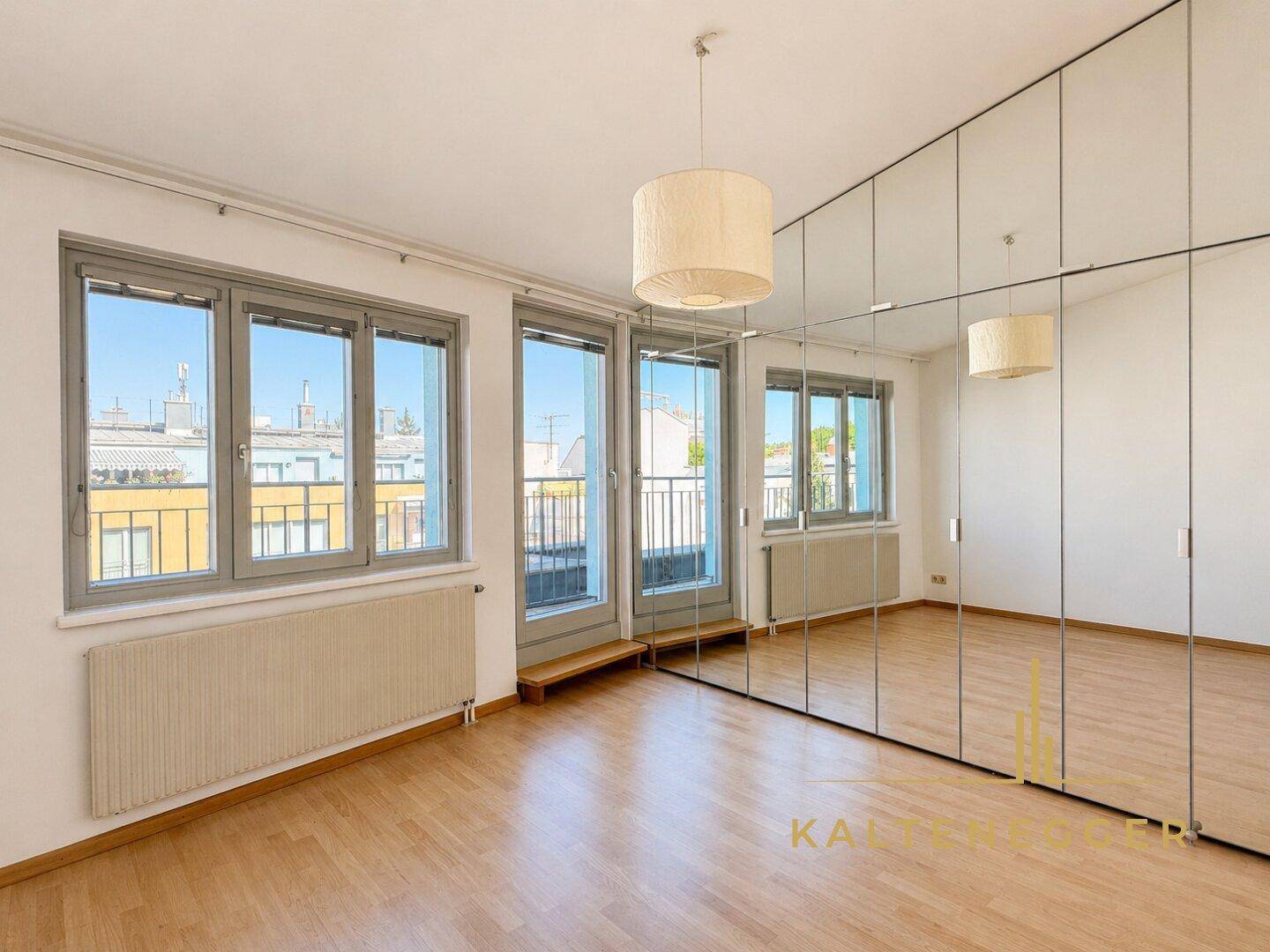 Schlafzimmer mit Parkettboden, Spiegelschränken und Zugang zu einem französischen Balkon.