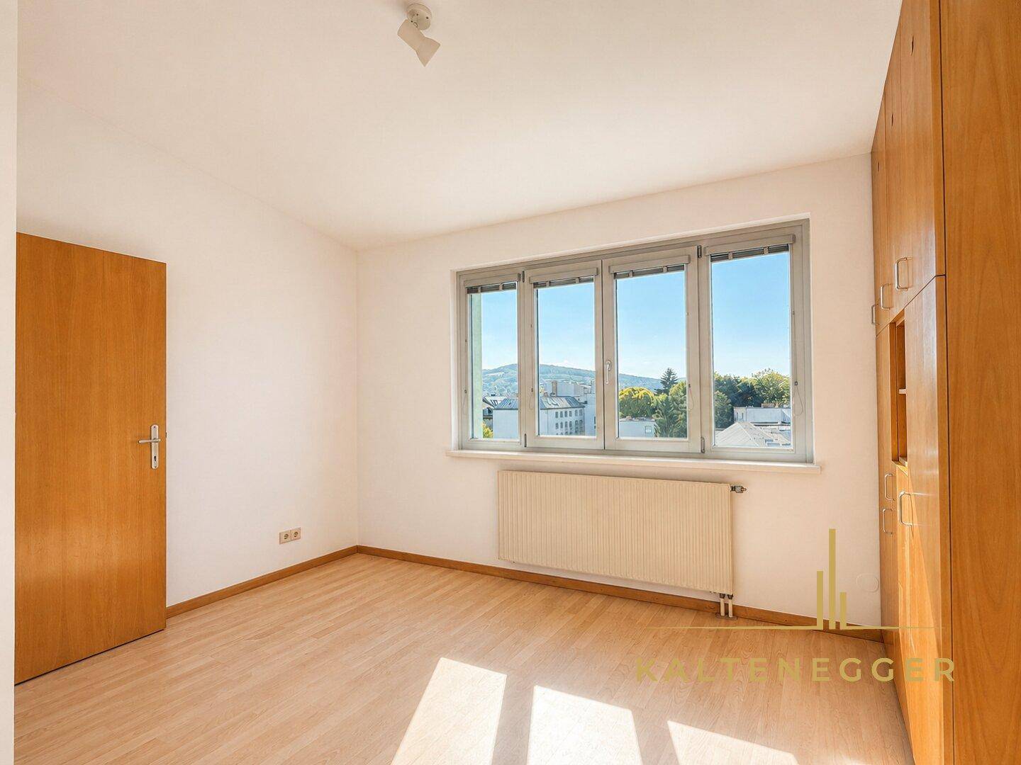 Helles Schlafzimmer mit Parkettboden, Holzeinbauschränken und Blick ins Grüne.