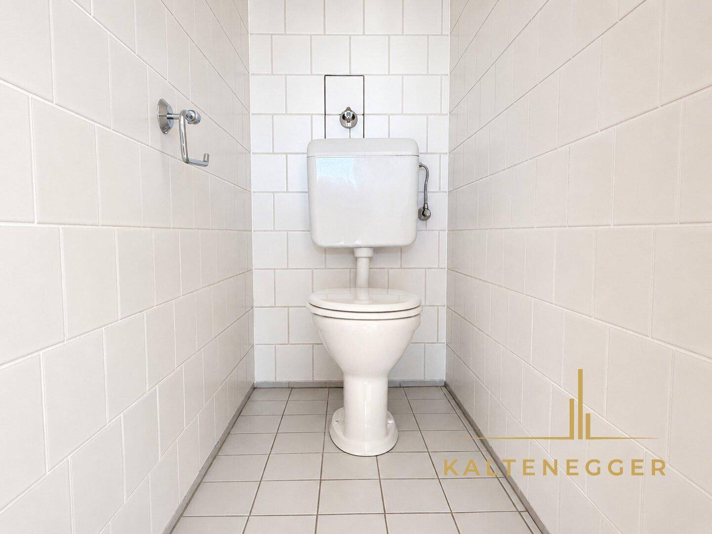 Separate Toilette mit Fliesen an Wänden und Boden, in schlichtem Design.