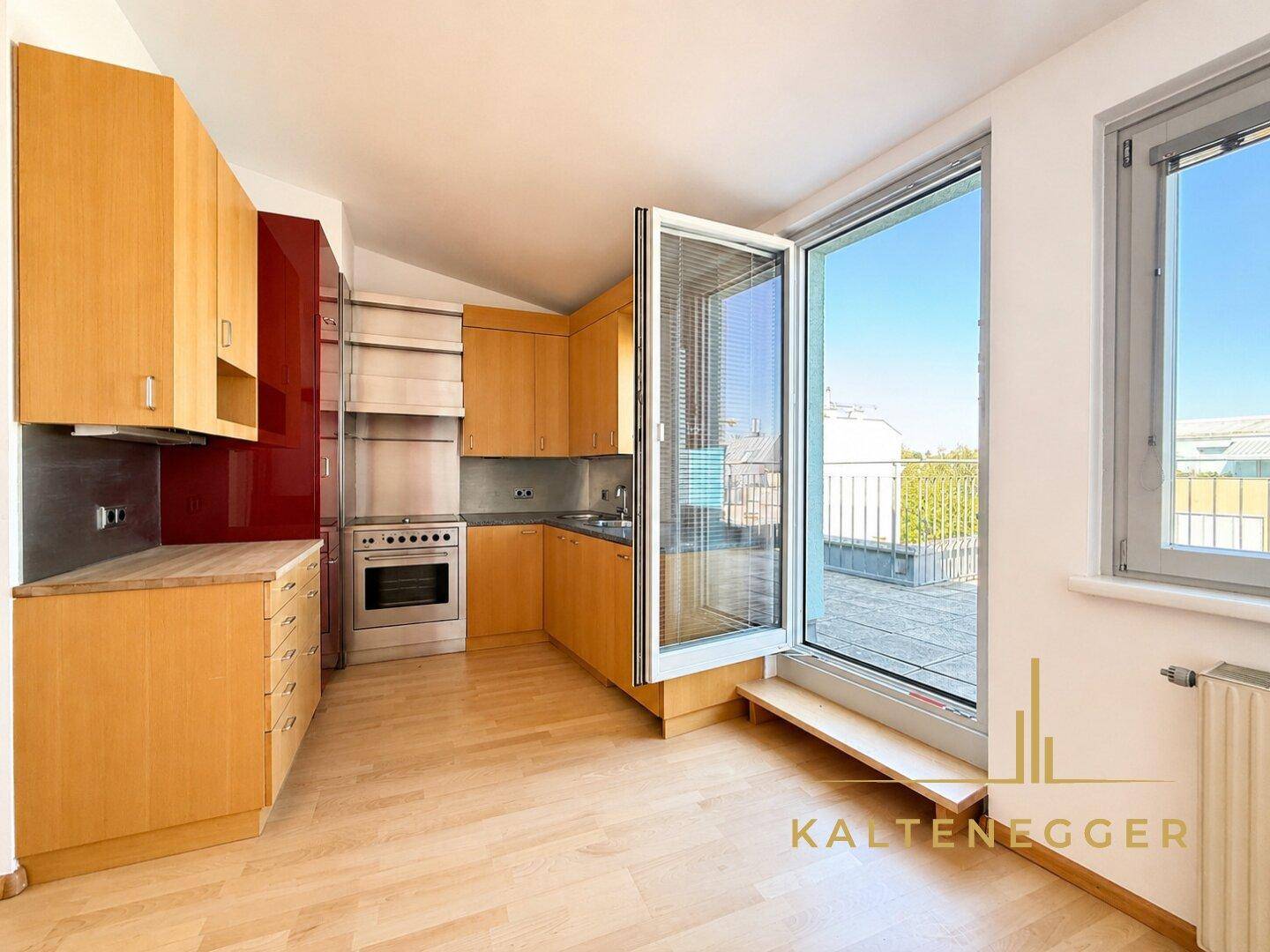 Helle Küche mit Holzelementen, Granitarbeitsplatte und Zugang zur Dachterrasse.