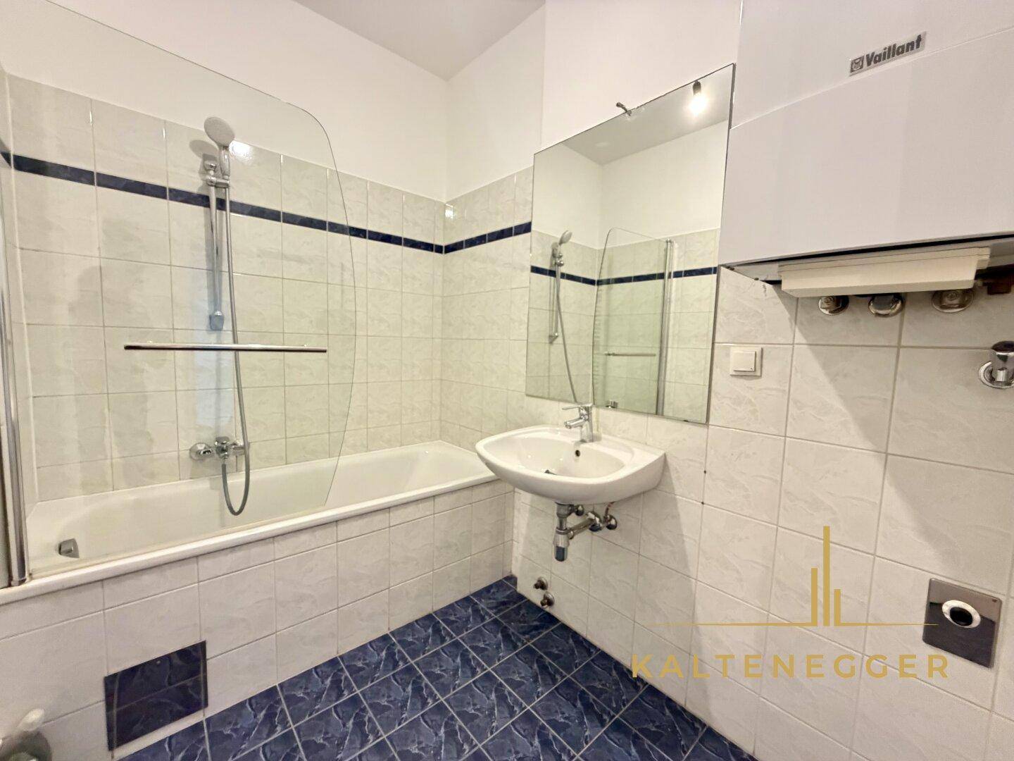 Badezimmer mit Badewanne, Waschbecken und blauen Bodenfliesen.