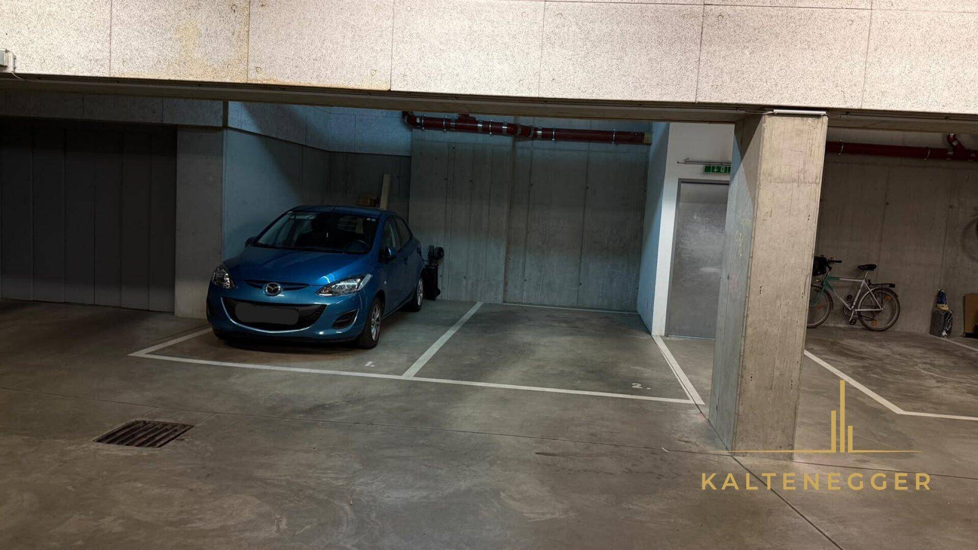 Ansicht der Tiefgarage mit einem blauen Auto auf einem markierten Stellplatz und robusten Betonstrukturen.