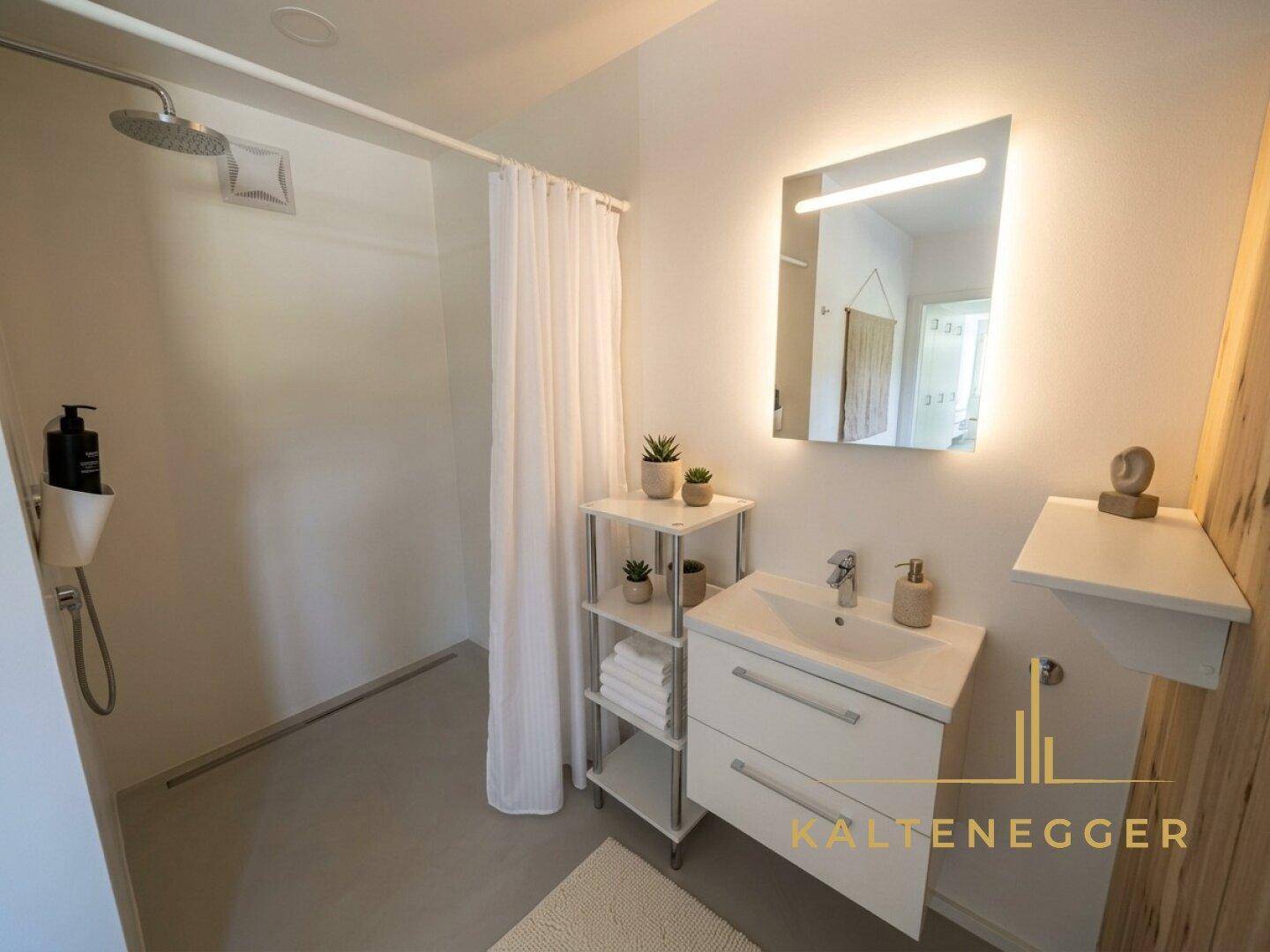 Modernes Badezimmer mit ebenerdiger Dusche, beleuchtetem Spiegel und weißem Waschtisch.