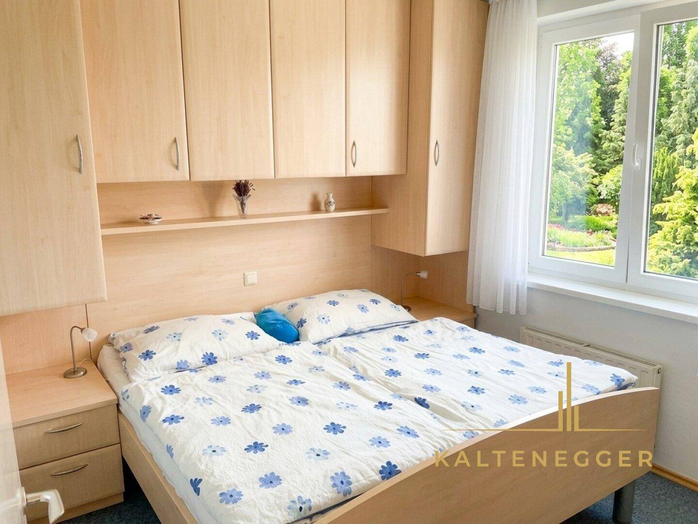 Schlafzimmer mit Doppelbett, integrierten Holzschränken über dem Bett und großem Fenster mit Grünblick.