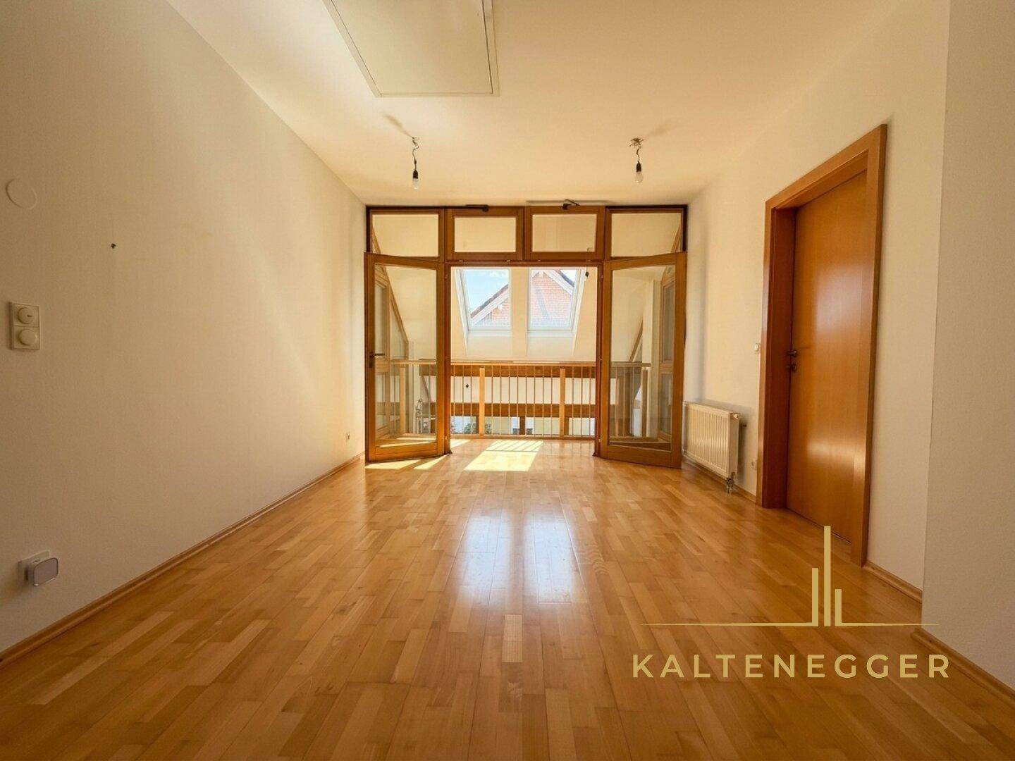 Heller Raum mit Holzboden und Zugang zu einem verglasten Bereich, möglicherweise eine Galerie oder offener Wohnraum.