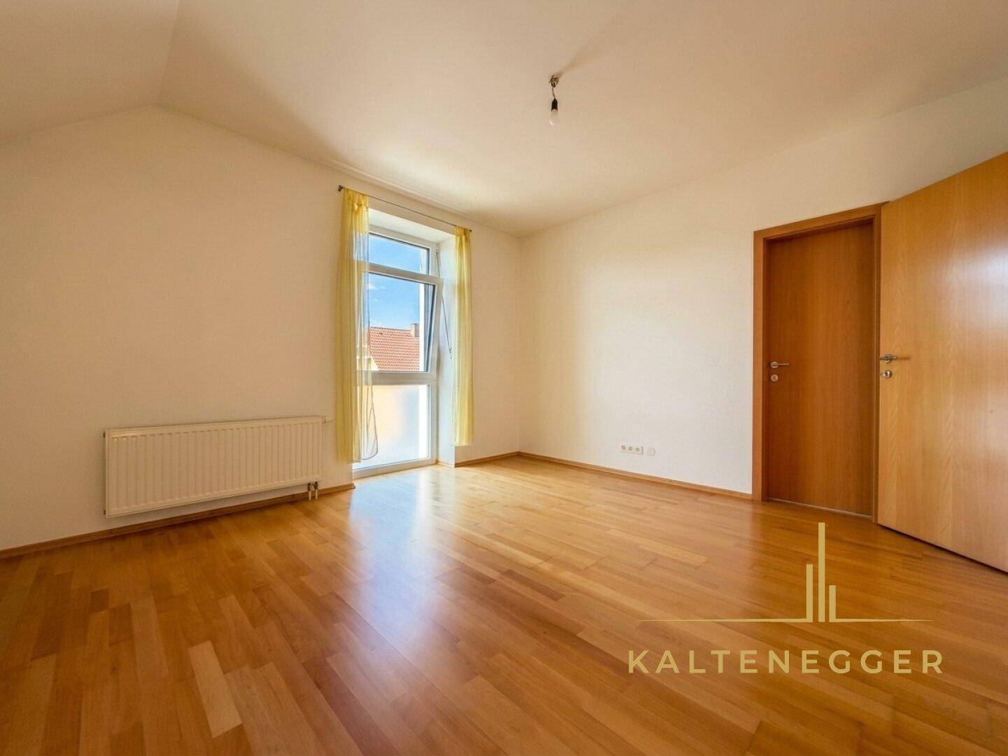 Leeres Schlafzimmer mit hellem Holzboden, großem Fenster und Heizkörper, bereit zur individuellen Gestaltung.