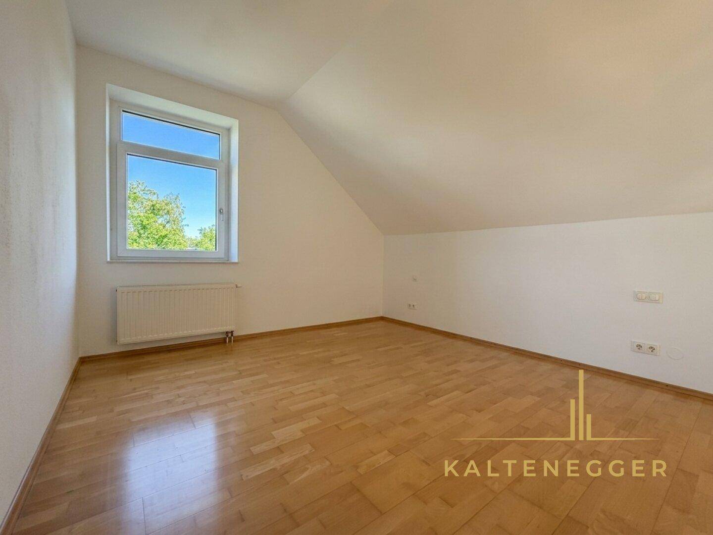 Geräumiges, leeres Schlafzimmer mit Holzboden, Fenster und Dachschräge, ideal für individuelle Einrichtung.