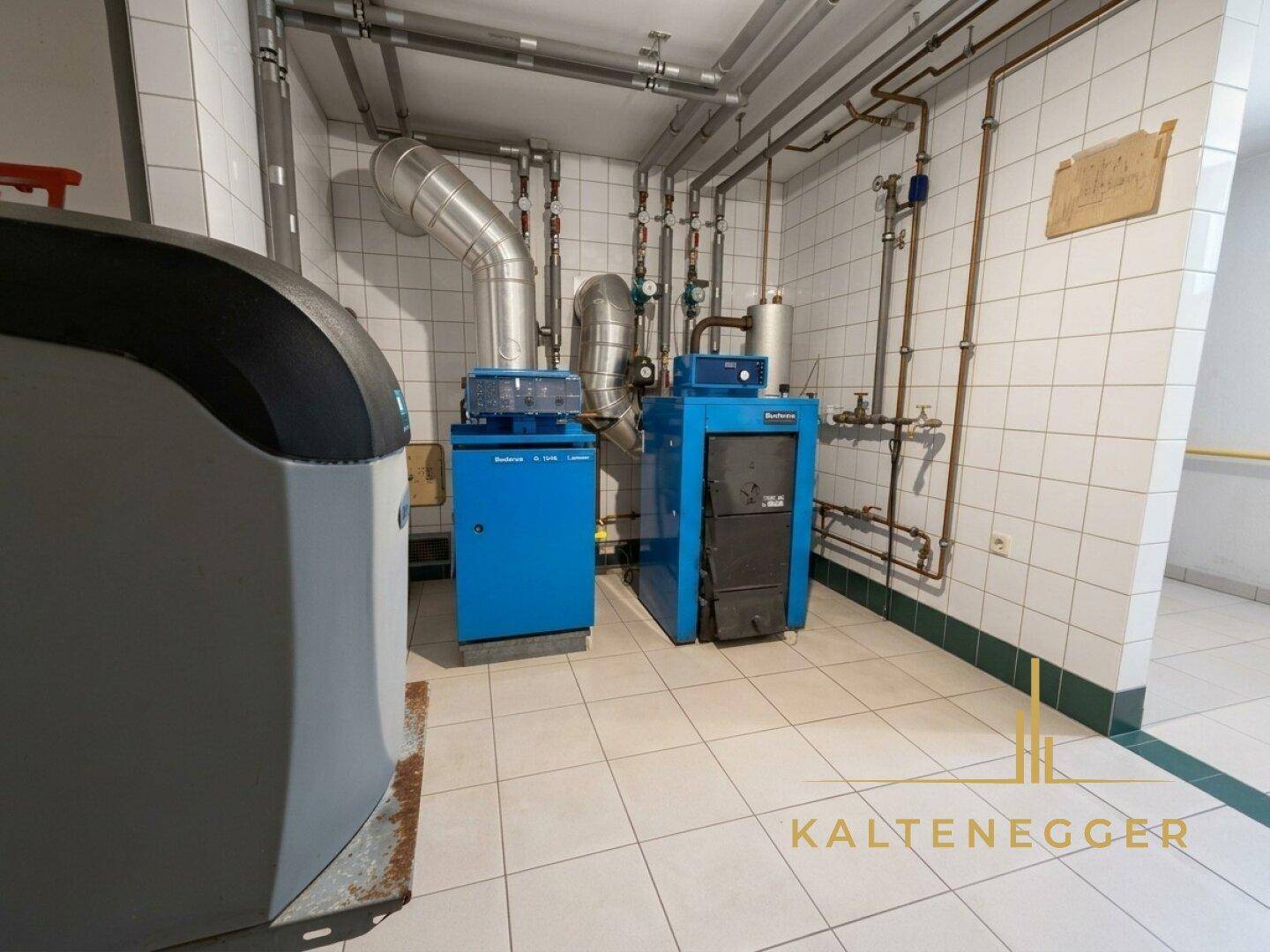 Heizungsraum mit moderner Heizungsanlage, umfangreichen Rohrleitungen und sauber gefliestem Boden.
