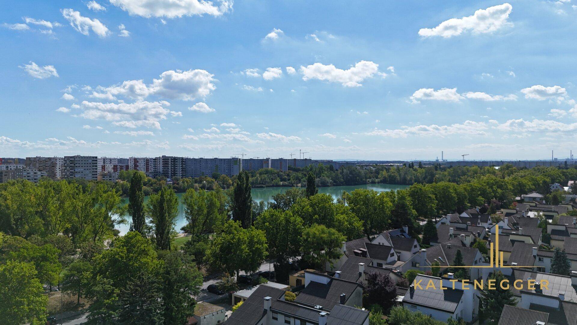 Panoramablick über eine Seenlandschaft mit üppigem Grün, Wohngebieten und einer fernen Stadtkulisse.